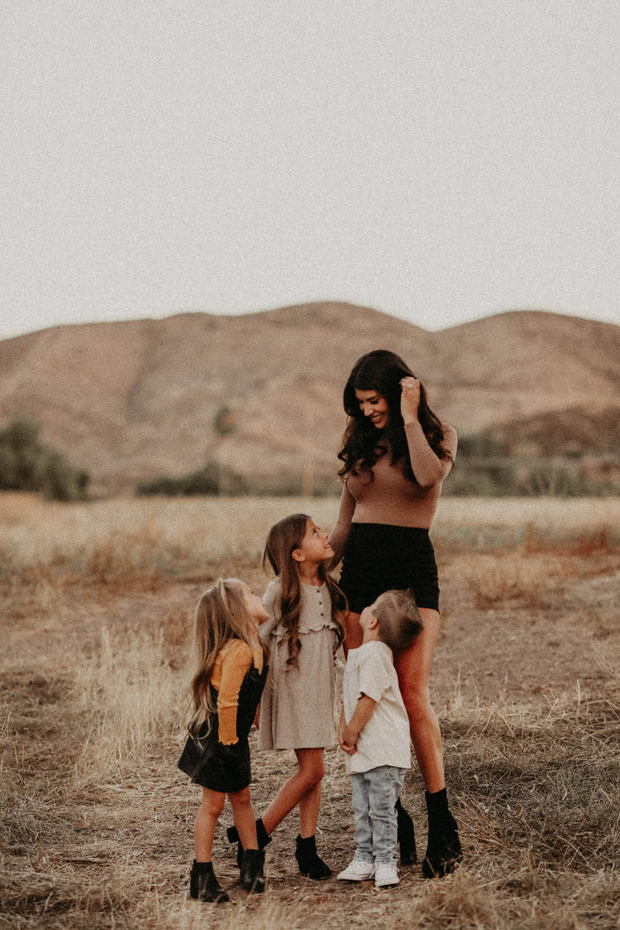 A woman with three children outdoors in a dry, mountainous area during sunset, engaging in a playful or affectionate moment.