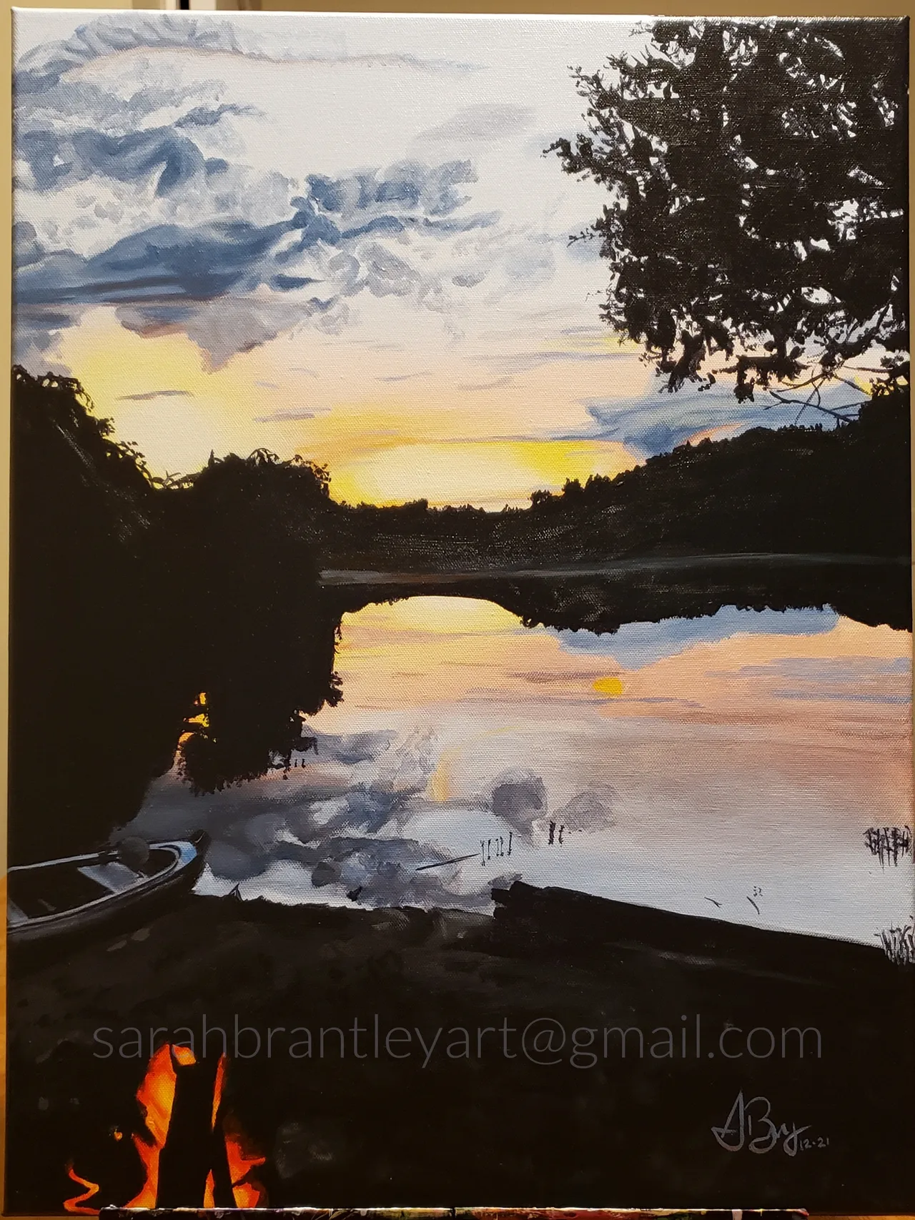 A painting of a sunset over a river at dusk with a small boat on the shore, trees and a bridge reflecting in the water.