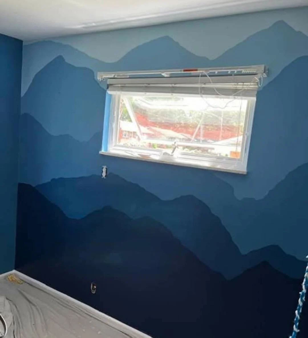 Blue mountain landscape painted on the wall of a room below a window.