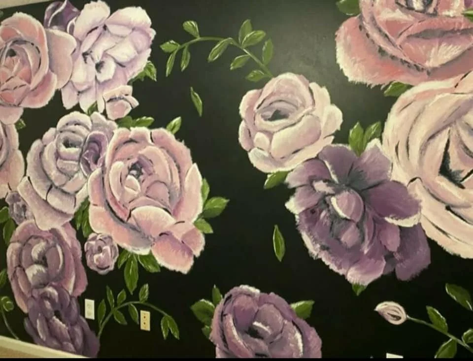 A wall painted with large pink and purple roses and green leaves on a dark background.
