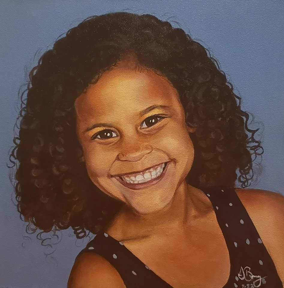 A young girl with curly hair smiling at the camera, wearing a black polka dot top, against a blue background.