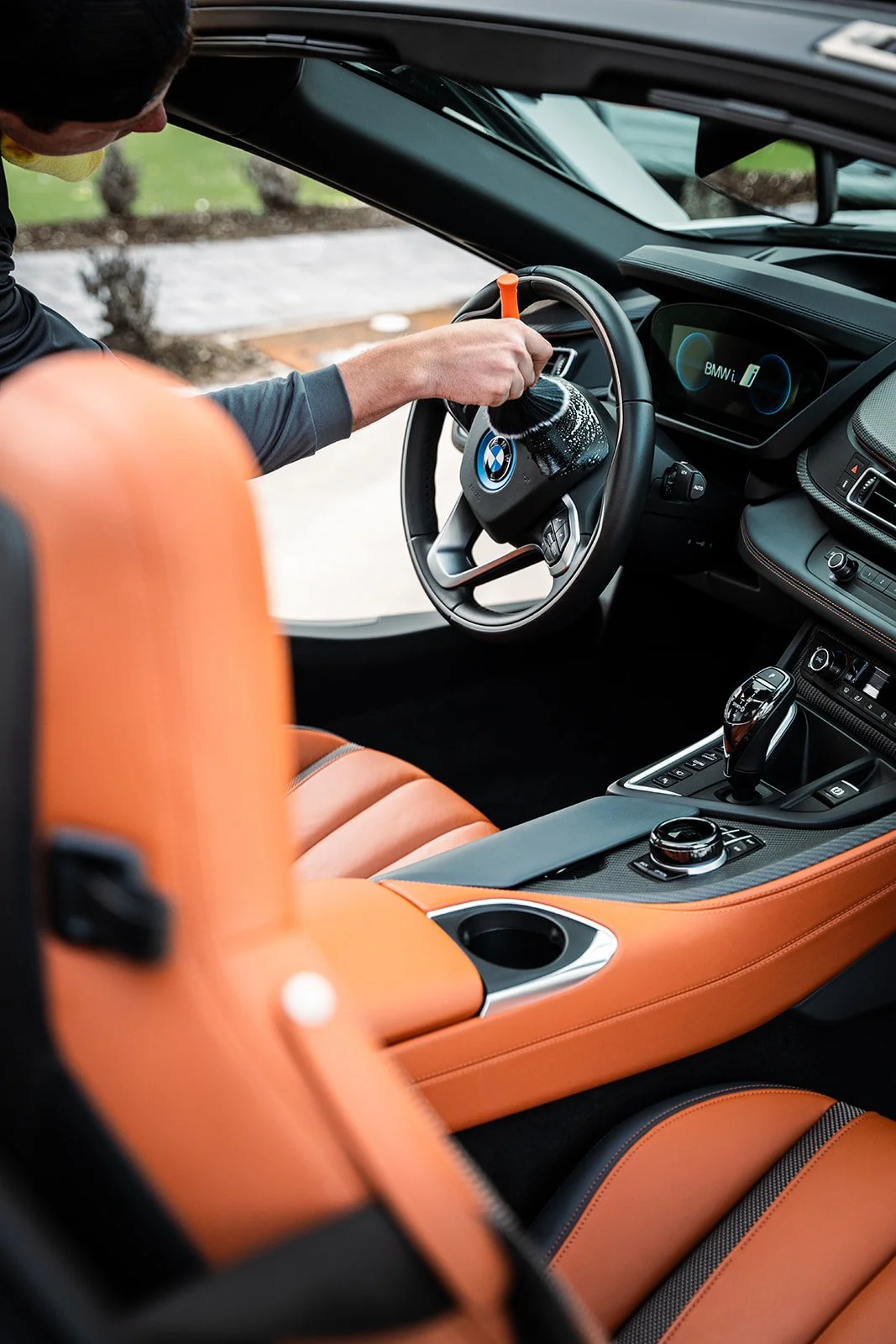 Person cleaning the steering wheel of a black BMW vehicle with an orange interior.