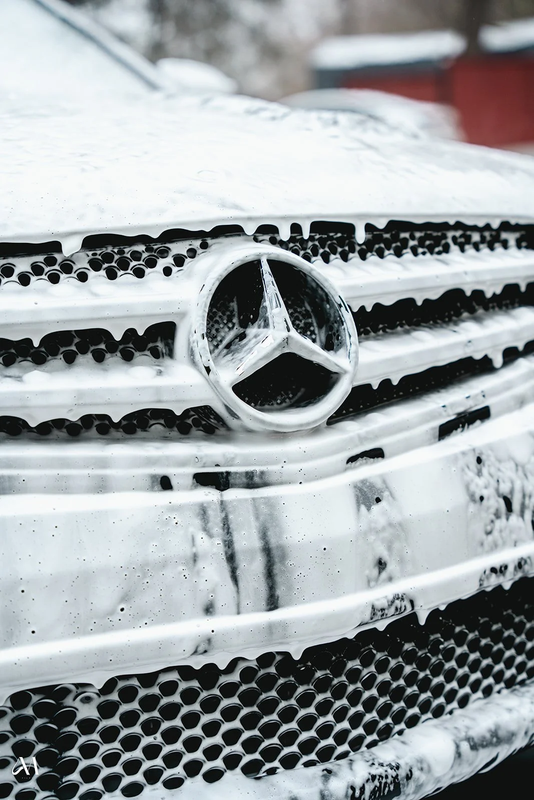 Close-up of a Mercedes-Benz emblem on a car's front grille covered in soap suds during washing.