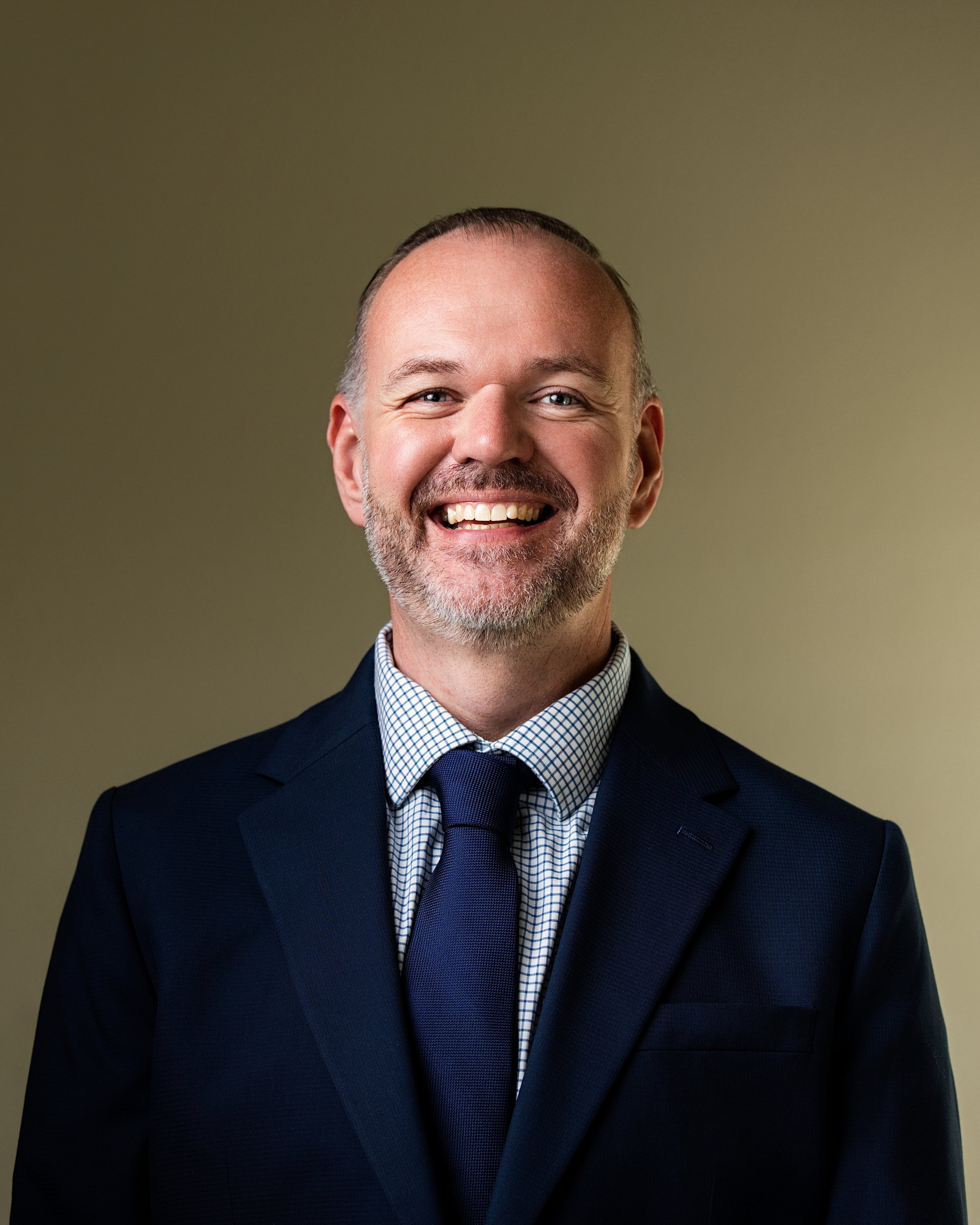 Professional corporate headshot photography of a business executive in a navy suit and tie on a clean studio background for branding, marketing, and company websites.