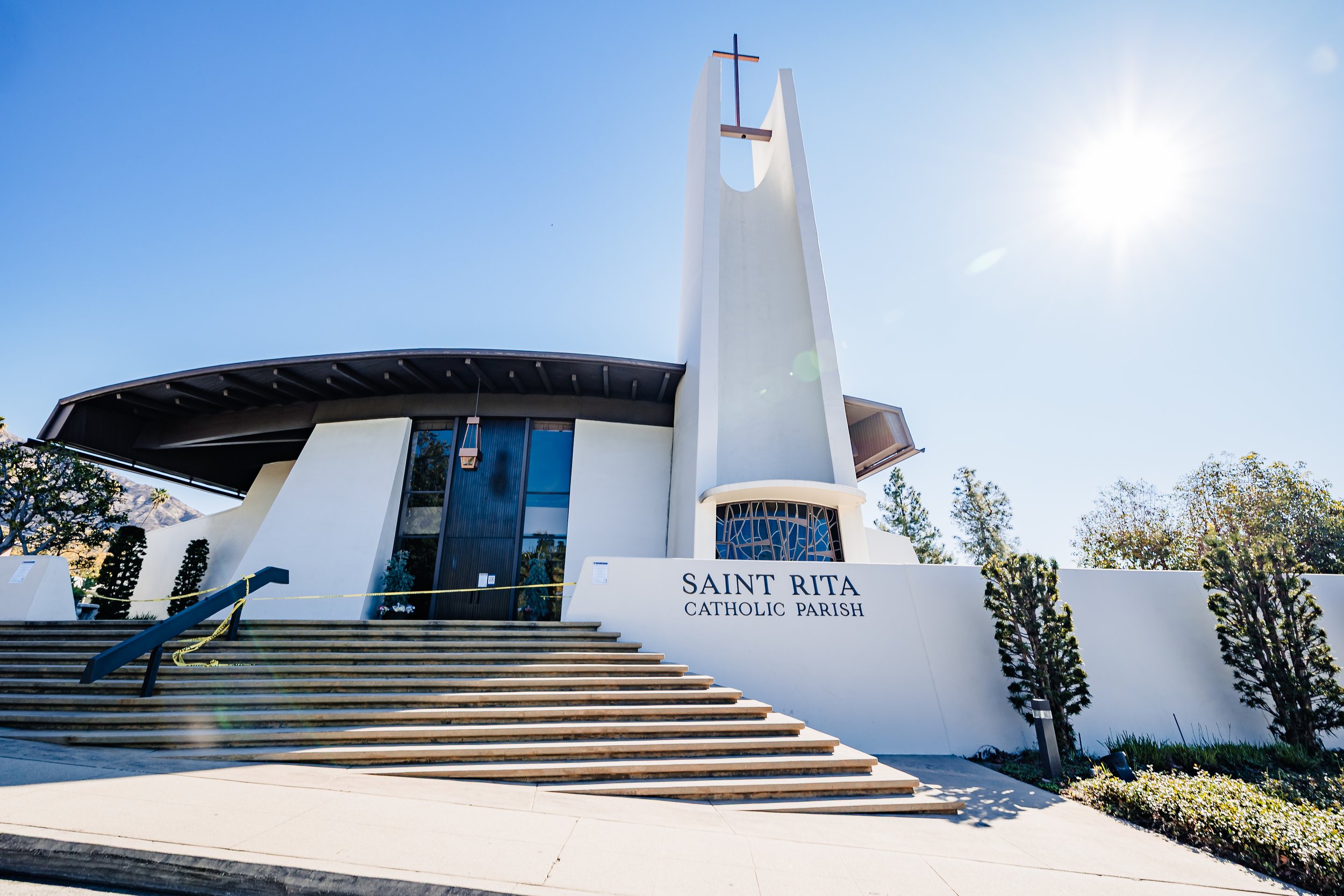 Architectural and commercial photography of Saint Rita Catholic Parish church exterior with modern design, steeple, and cross under clear blue sky for nonprofit and organizational marketing.