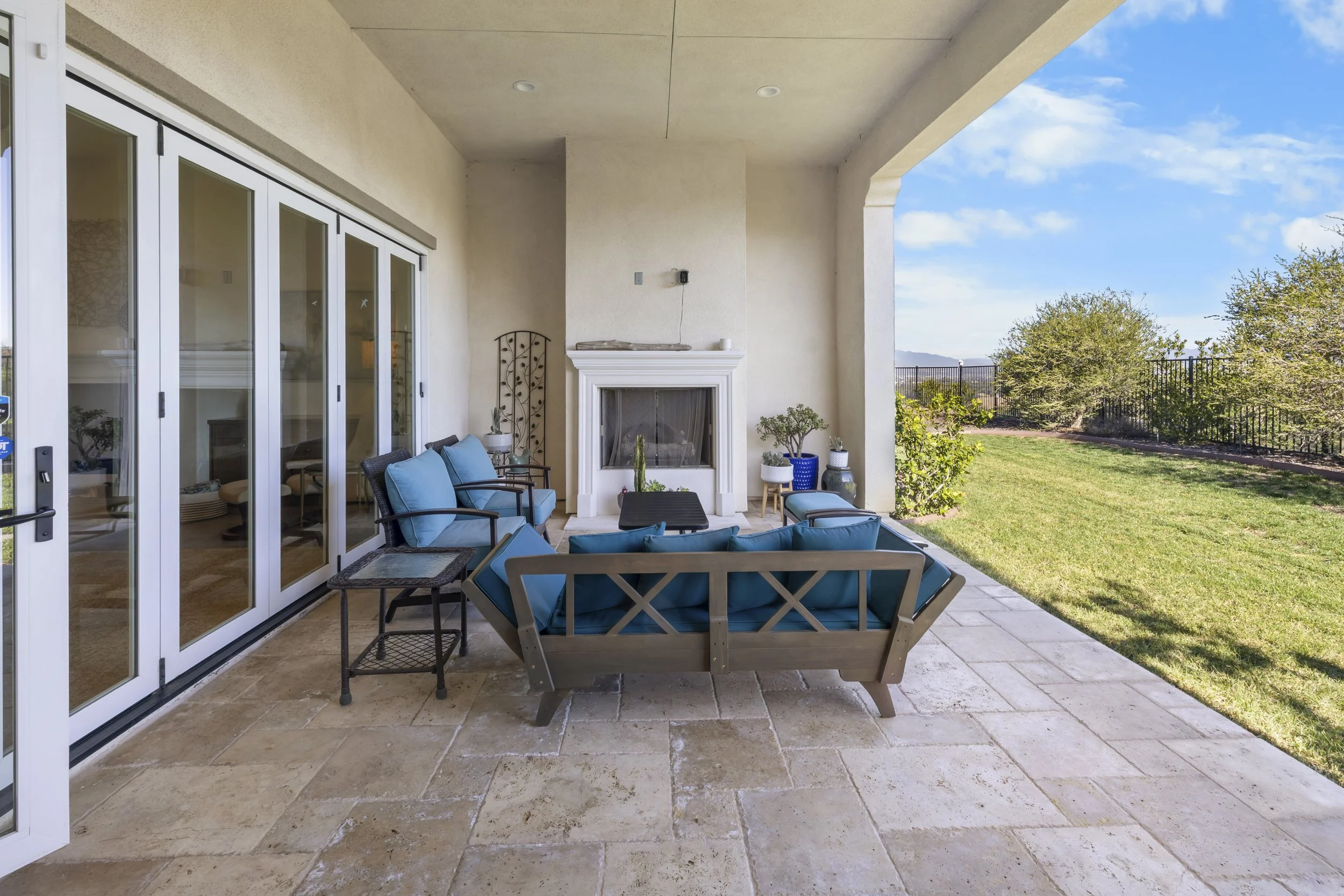 Luxury real estate photography of a covered outdoor patio with tiled flooring, fireplace, modern seating, and landscaped views for high-end property marketing.
