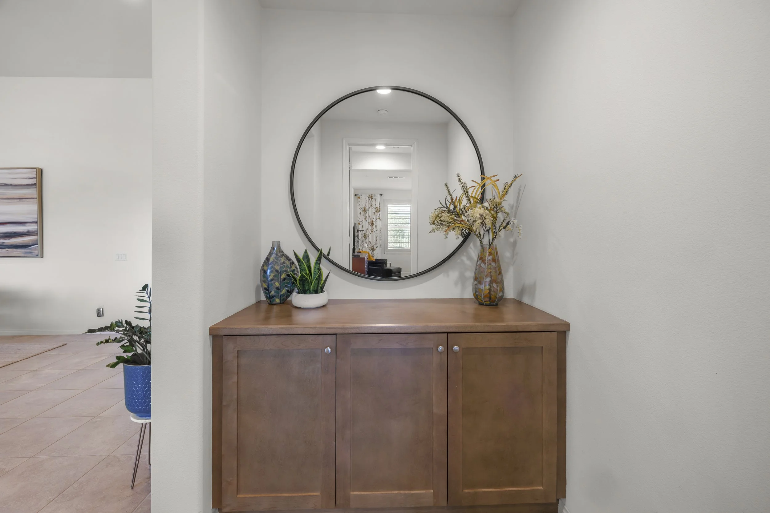 High-quality real estate photography of a modern entryway featuring a wooden console table, decorative accents, and circular mirror for residential listing and interior marketing.
