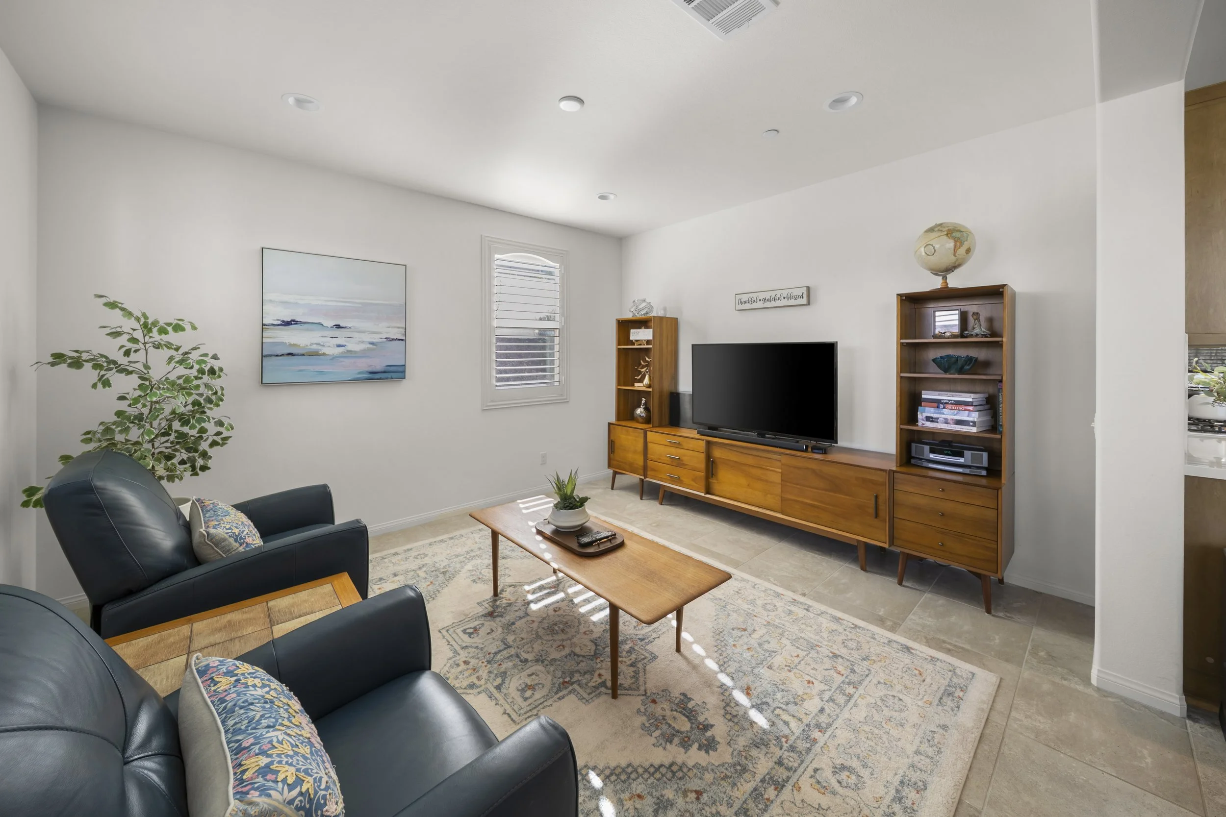 Wide-angle real estate interior photography of a bright living room with modern seating, wood furnishings, natural light, and clean white walls for property listings and marketing.