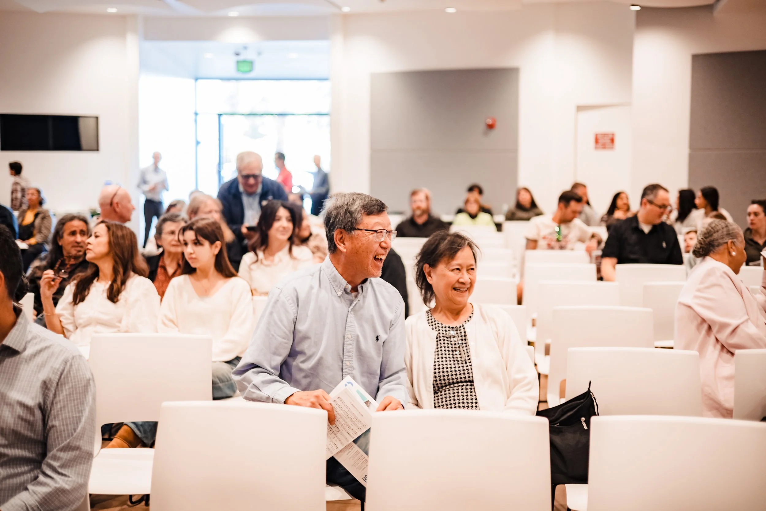 Professional conference photography of attendees smiling and engaged in a well-lit seminar room for corporate marketing and promotional use.