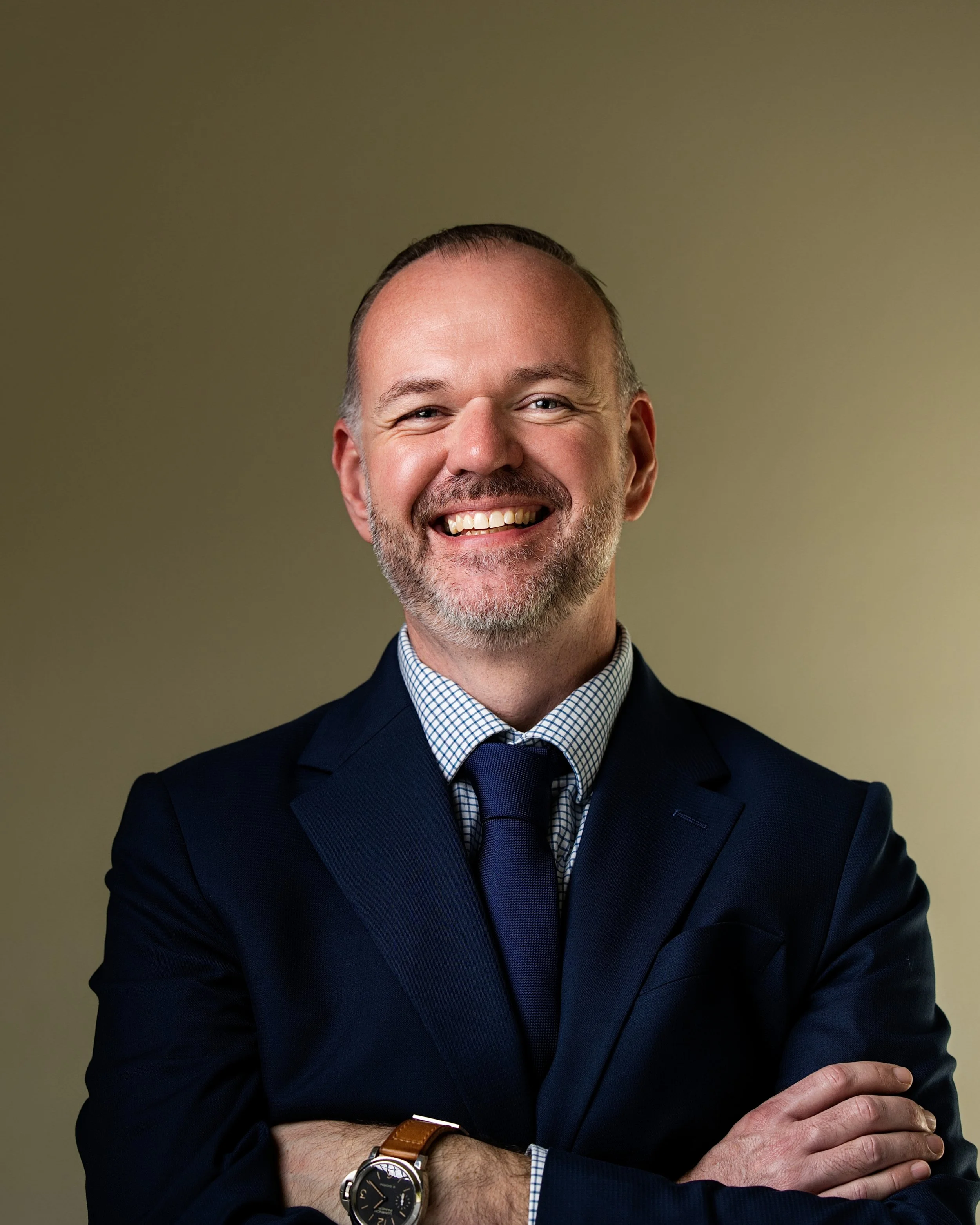 High-end corporate headshot of a smiling executive with arms crossed in a navy suit for leadership branding, LinkedIn profiles, and professional business marketing.