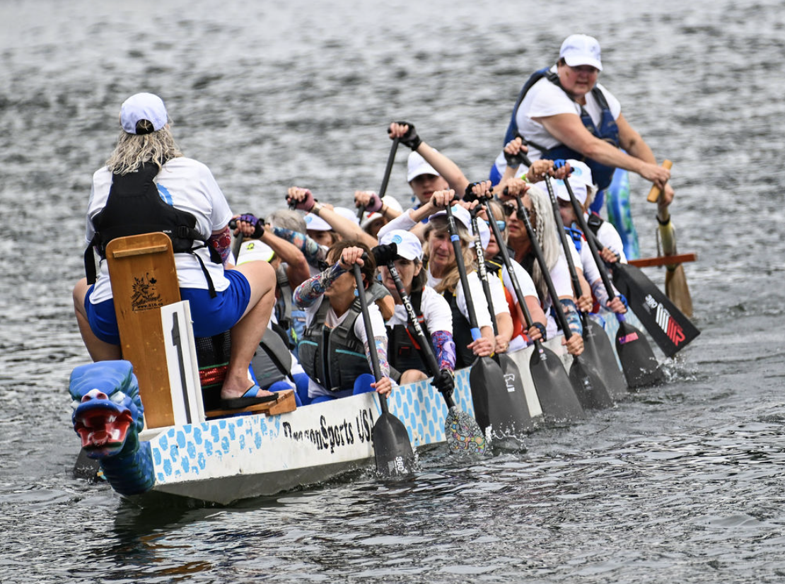 Image of the North Coast Paddling Club team racing in a dragon boat on the river in the Pacific Northwest.