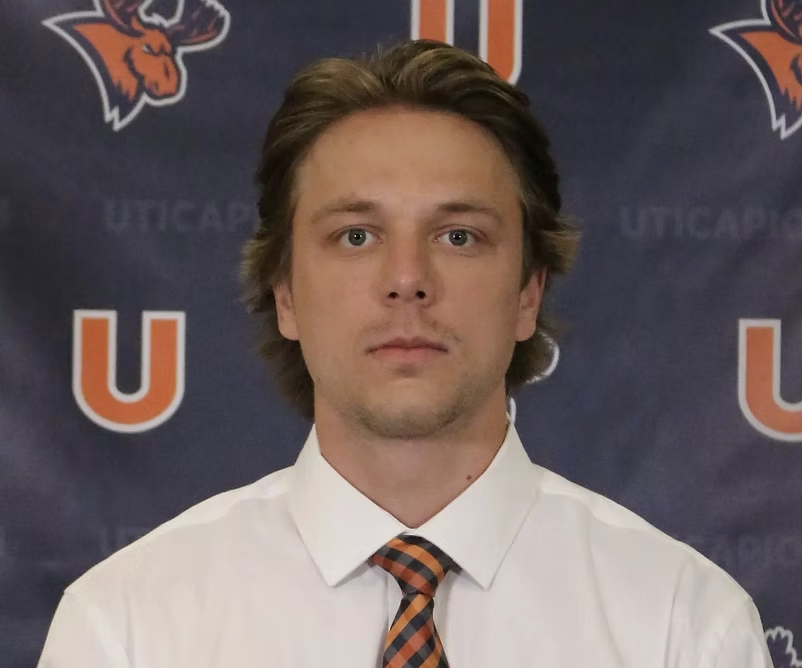 A young man with light brown hair, wearing a white shirt and striped tie, standing in front of a backdrop with the University of Utah logo and colors.