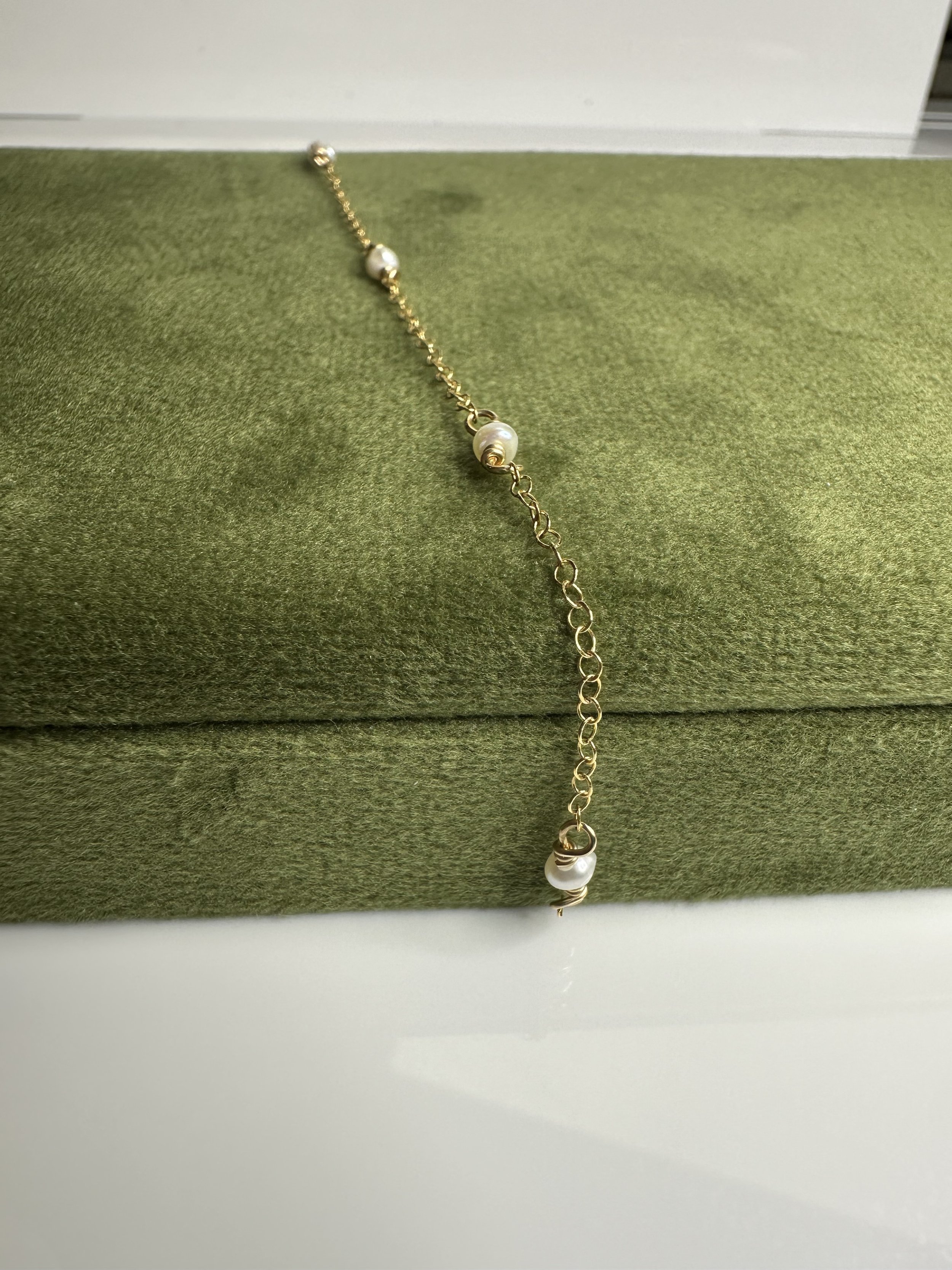 Gold chain necklace with pearl accents draped over a green textured jewelry box.
