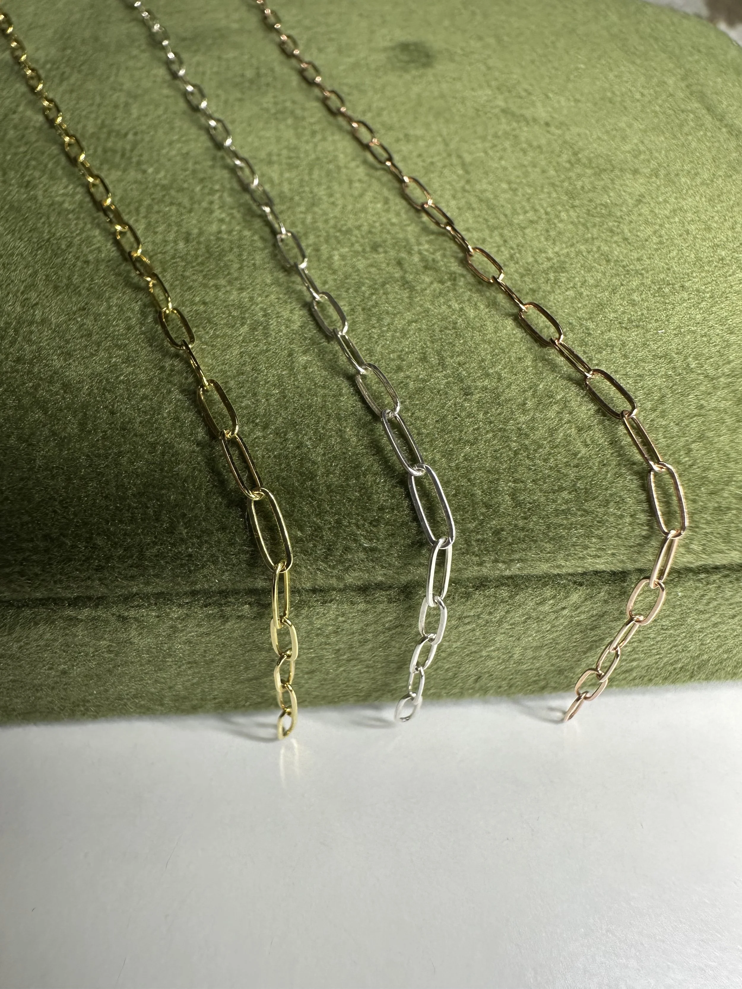 Three chain necklaces in gold, silver, and rose gold colors displayed on a green textured surface.
