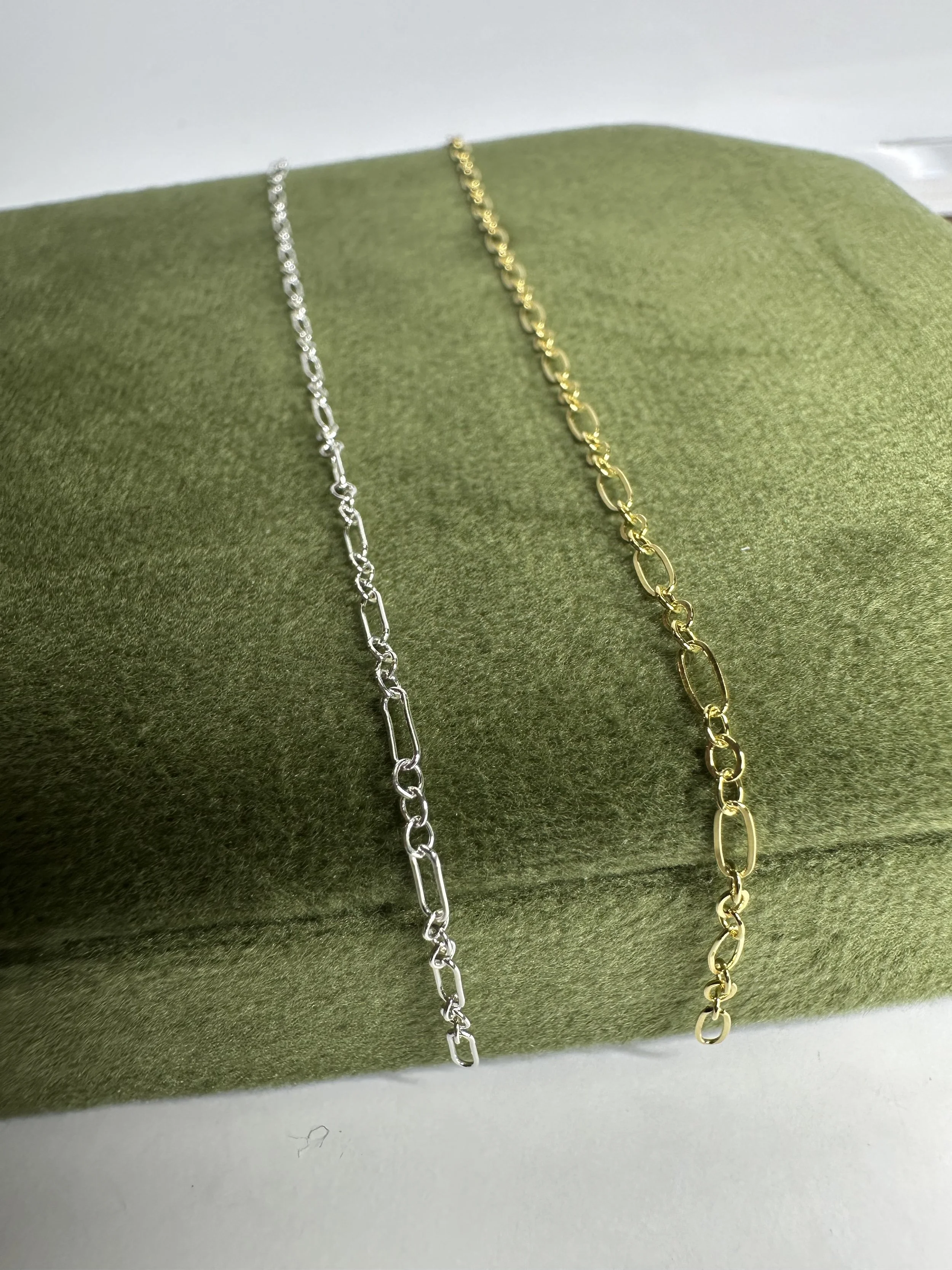 Silver and gold chain necklaces displayed on a green fabric surface.