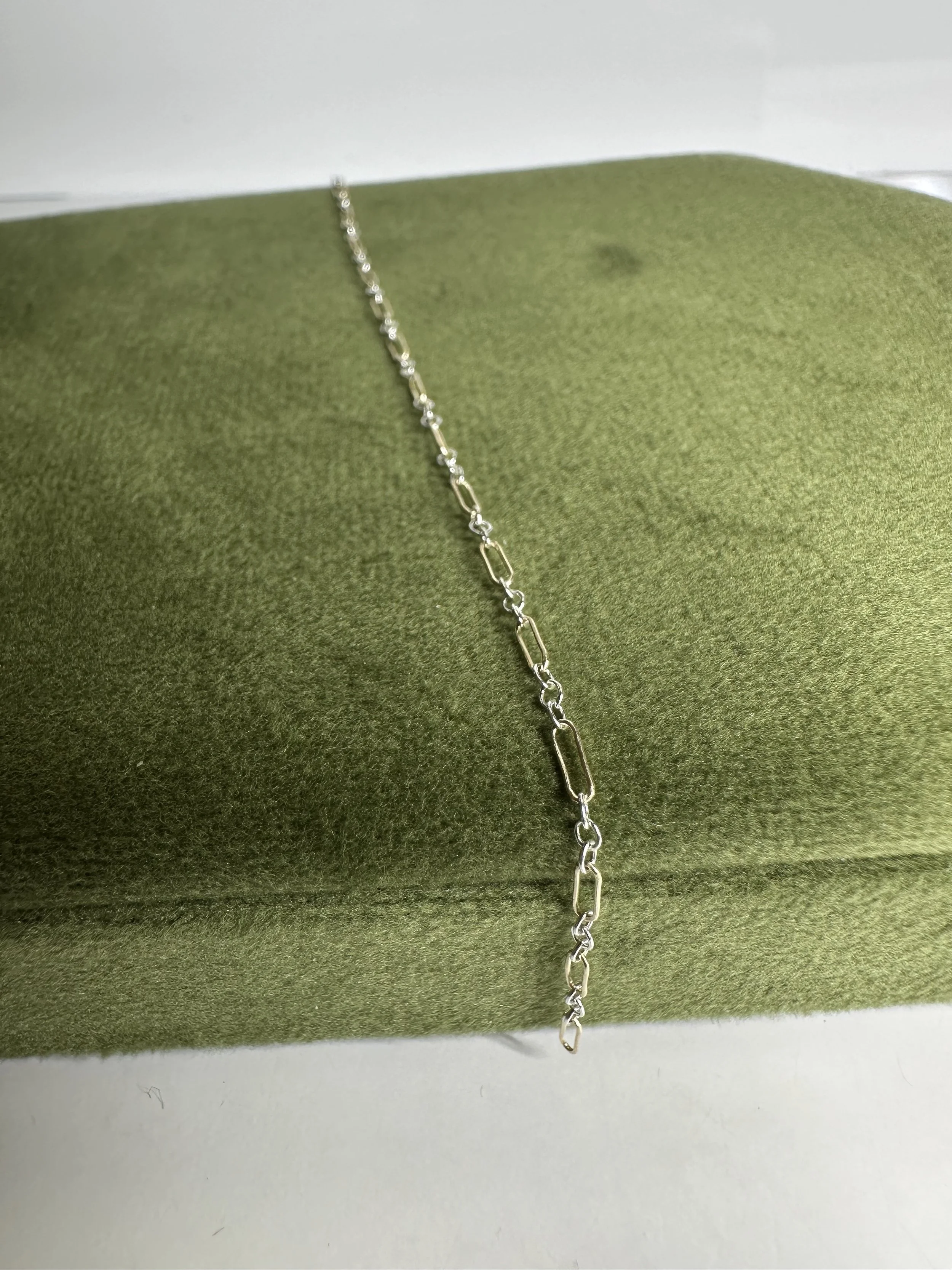 Silver chain necklace on a green textured jewelry display
