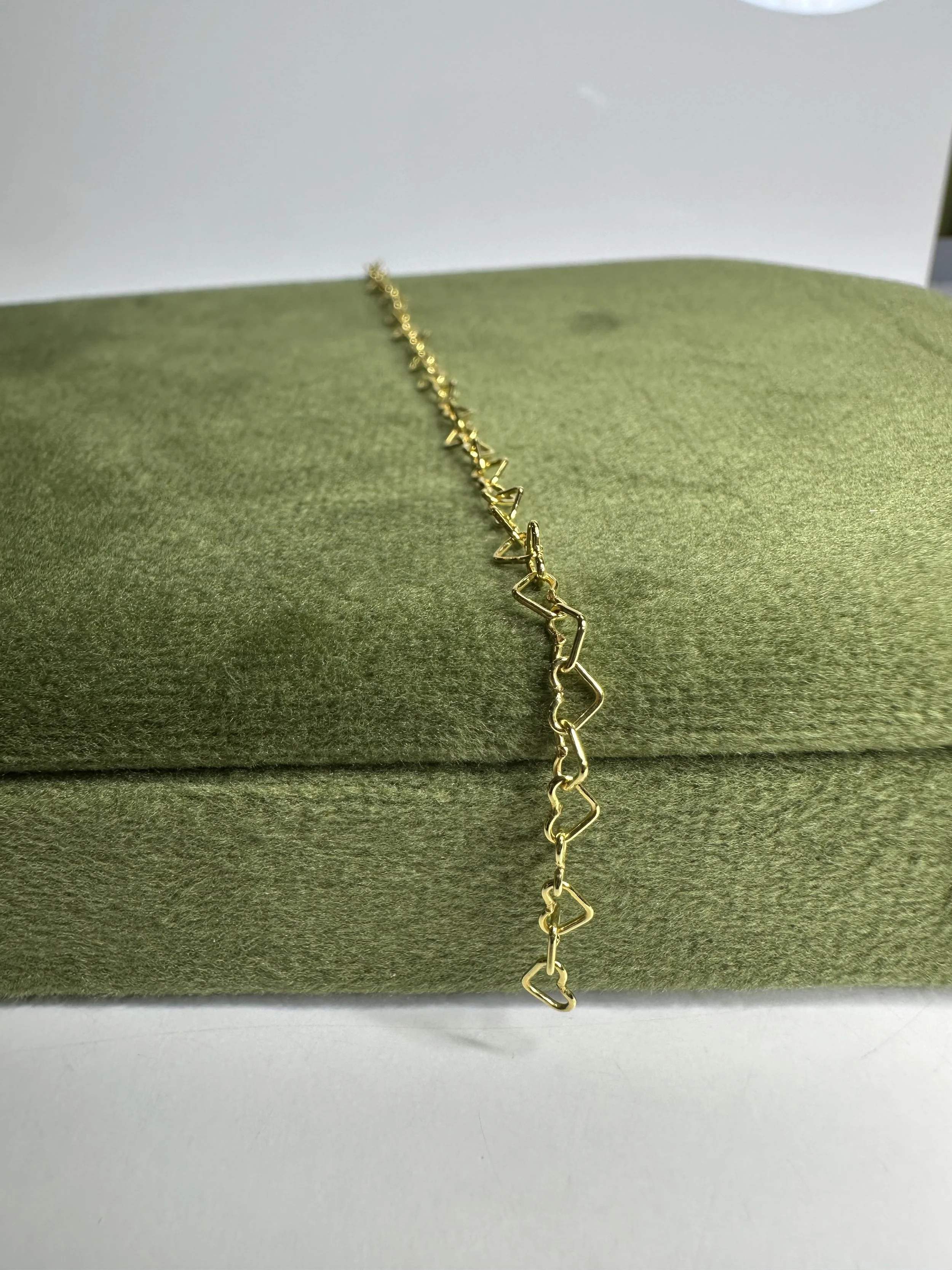 Gold bracelet with abstract geometric linked shapes, resting on a green velvet jewelry display.