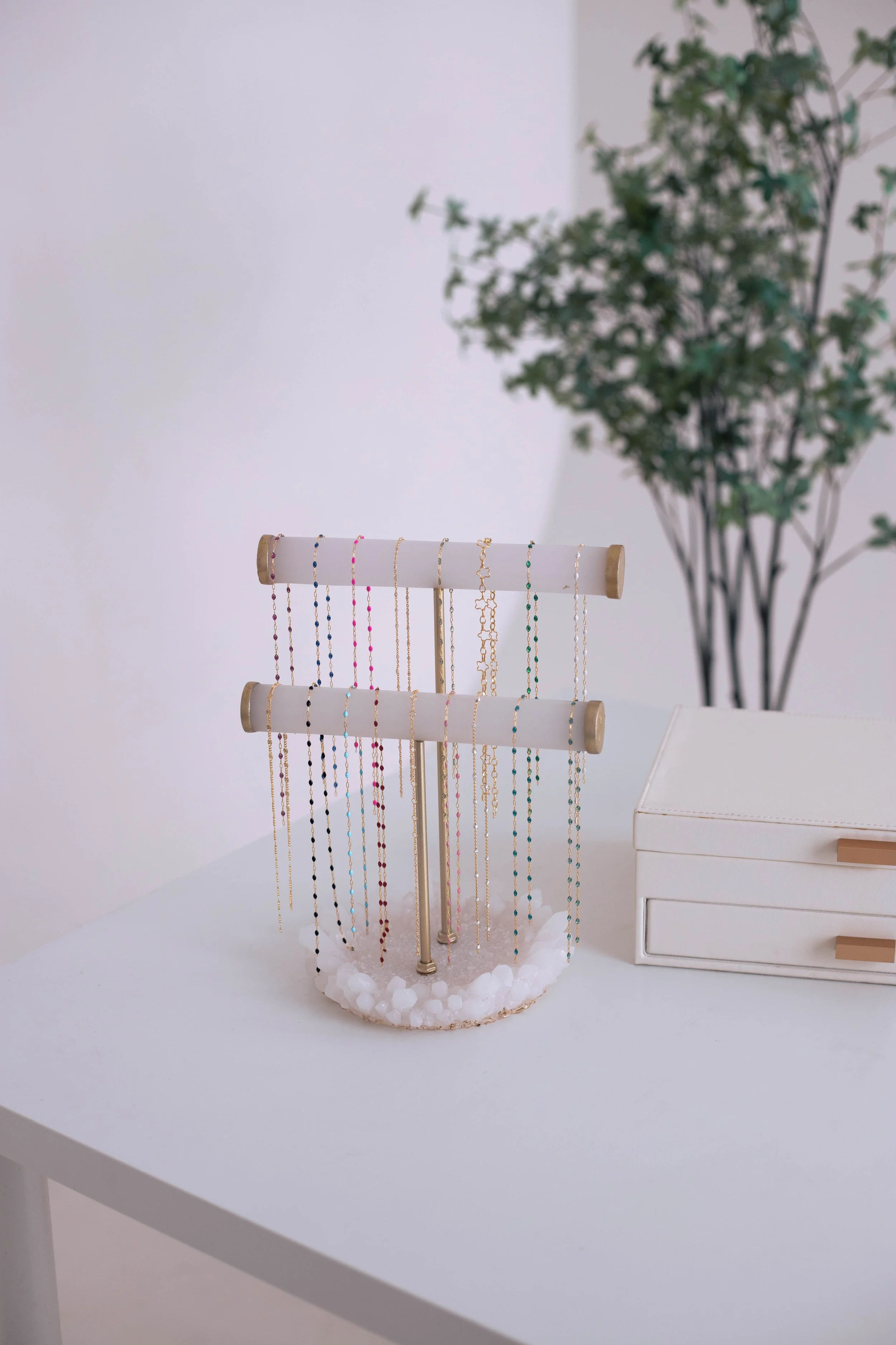 Jewelry display stand with colorful necklaces on a white table, with a plant in the background.