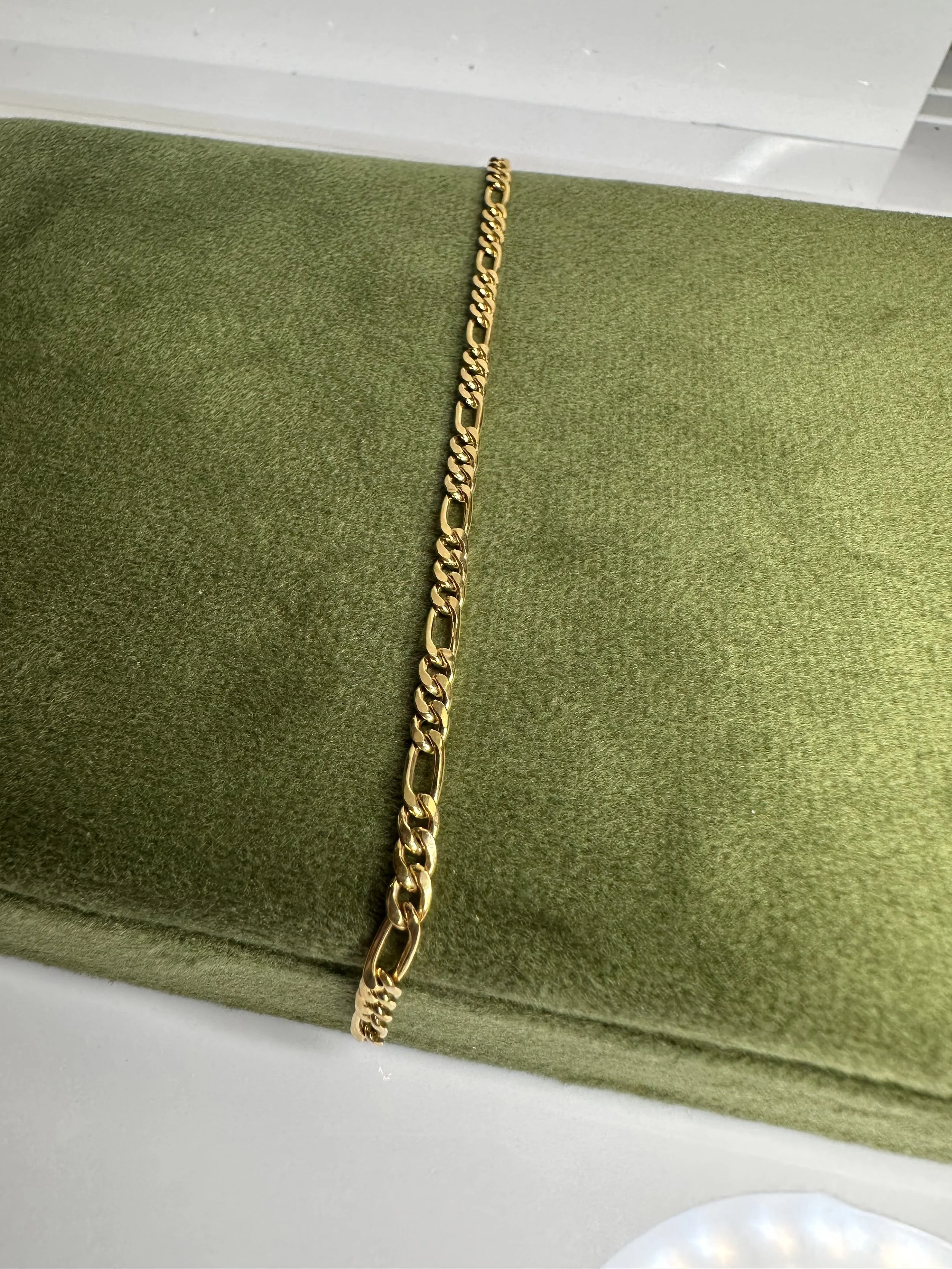 Gold chain necklace displayed on a green cushioned surface.
