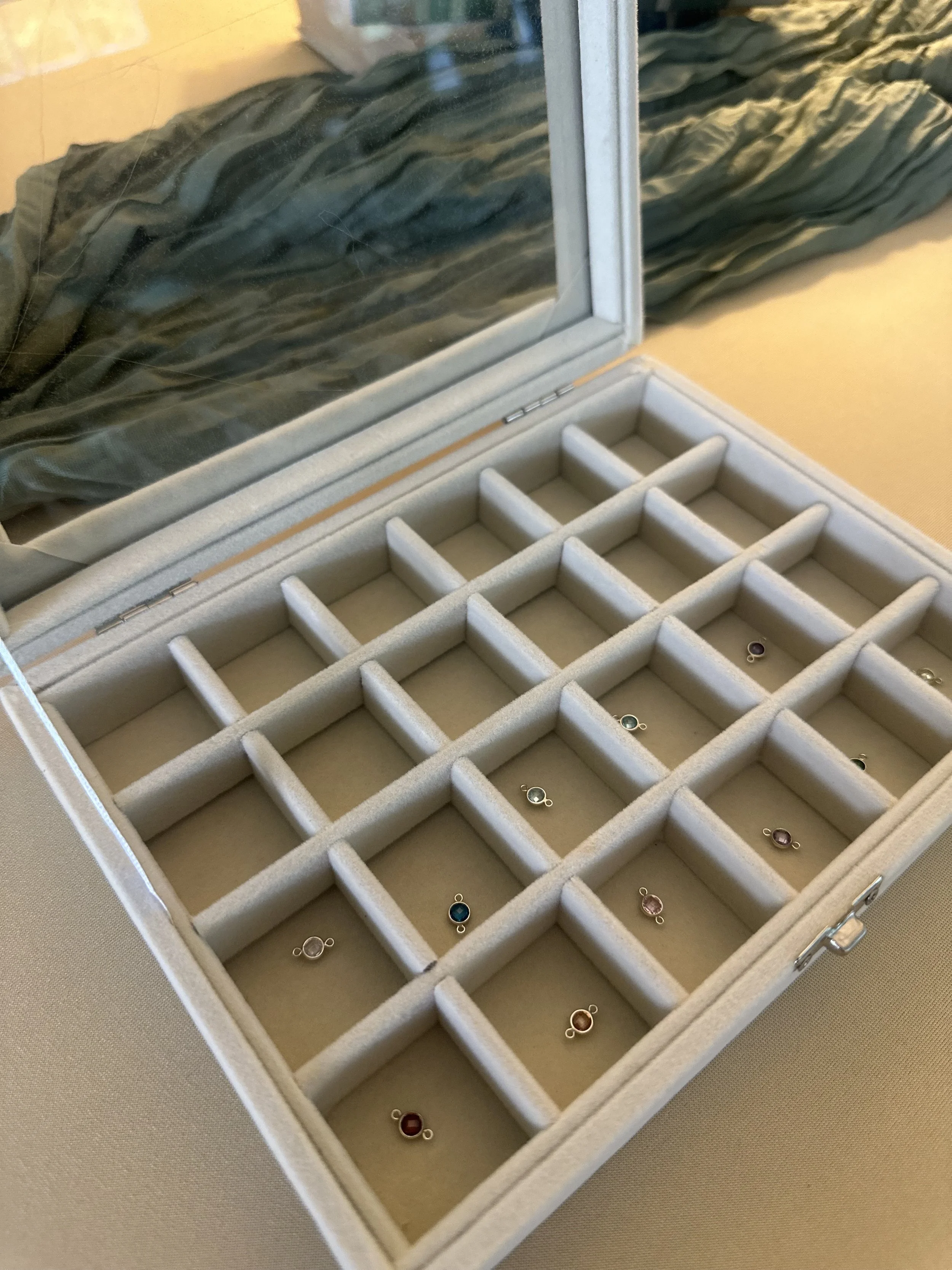 An open jewelry box with a mirror, displaying multiple small rings with colorful stones, arranged in compartments.