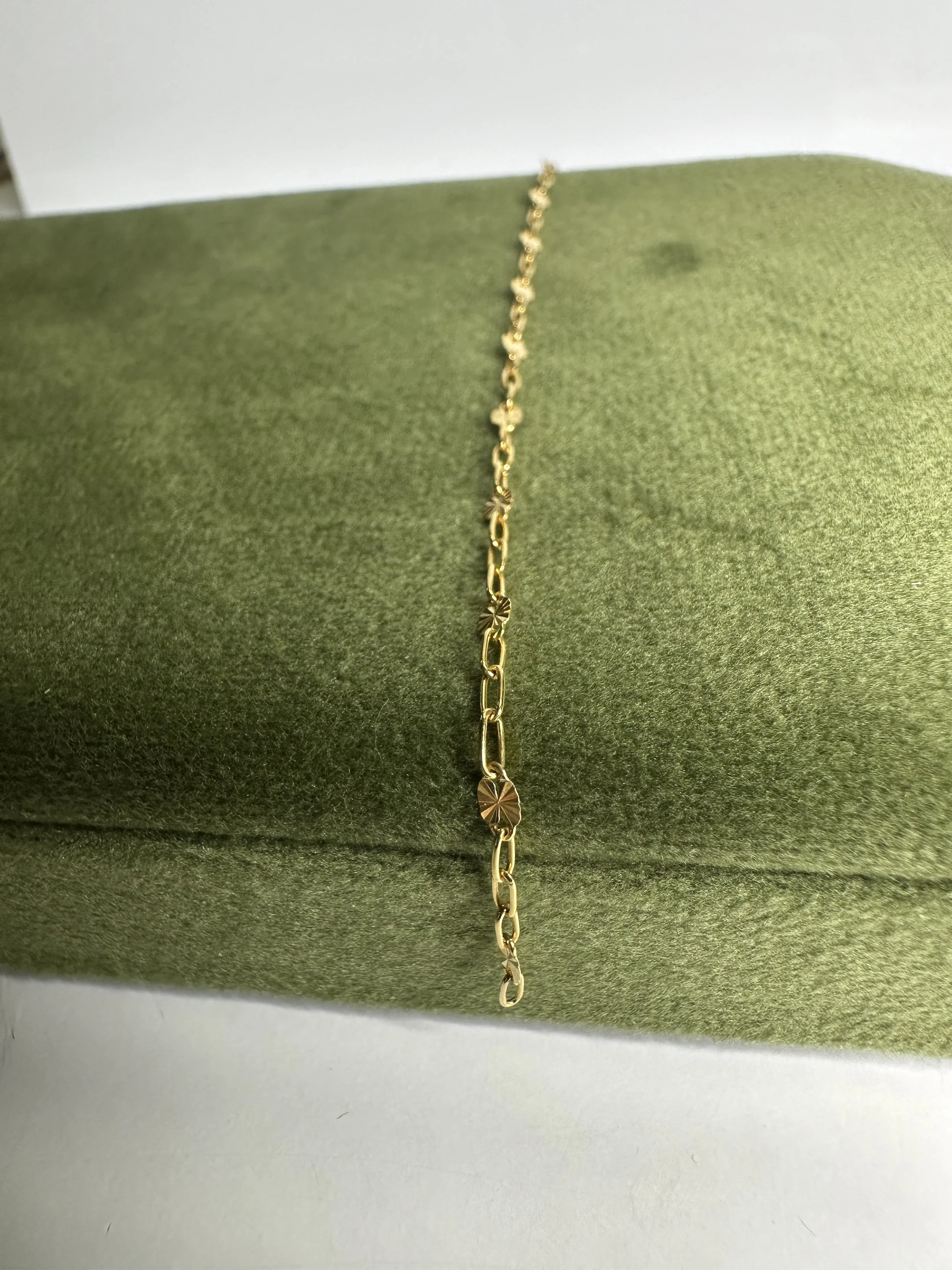 Gold bracelet with small circular decorative elements, resting on a green velvet cushion.