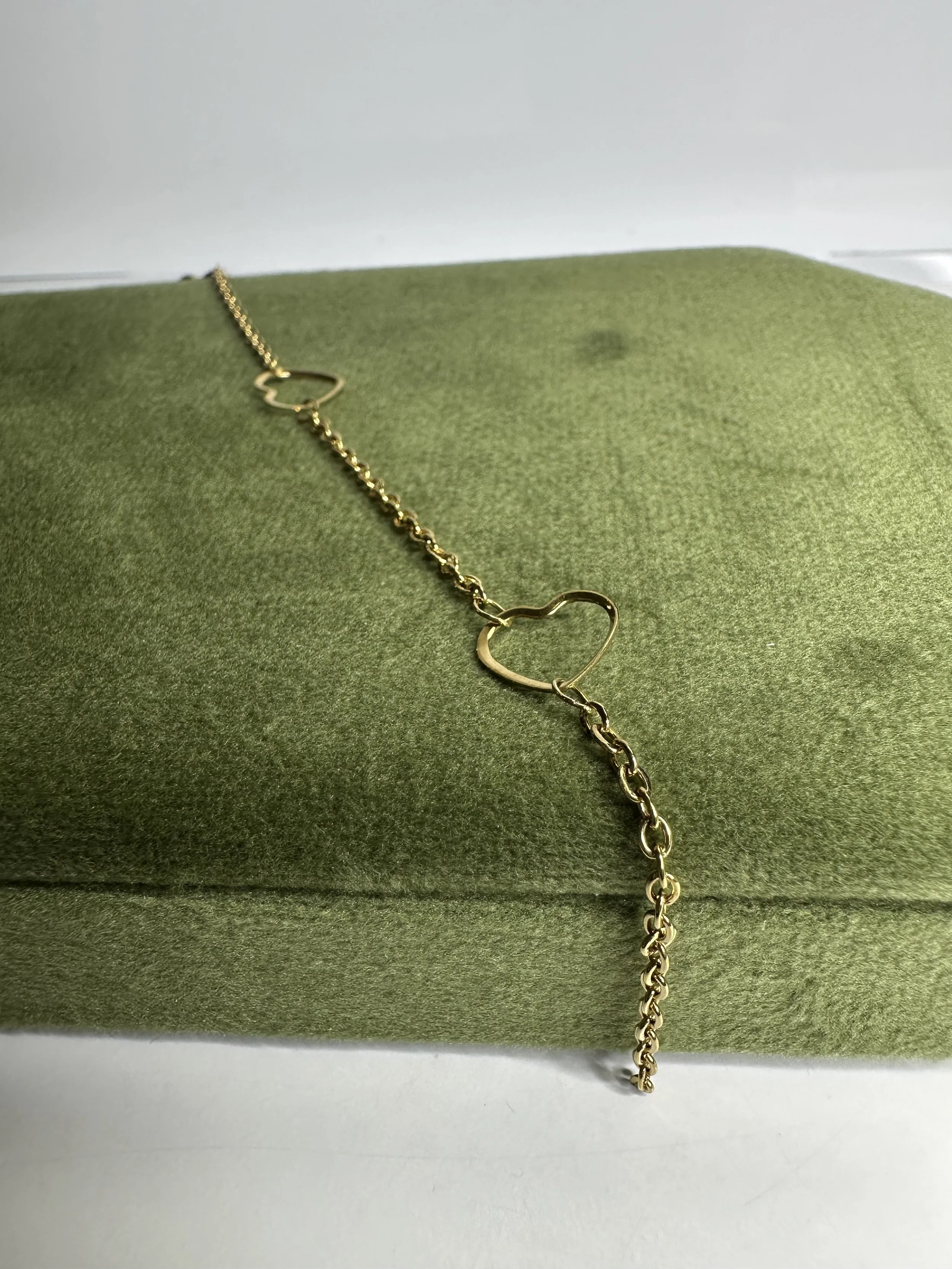 A gold chain bracelet with heart-shaped links, placed on a green textured surface.
