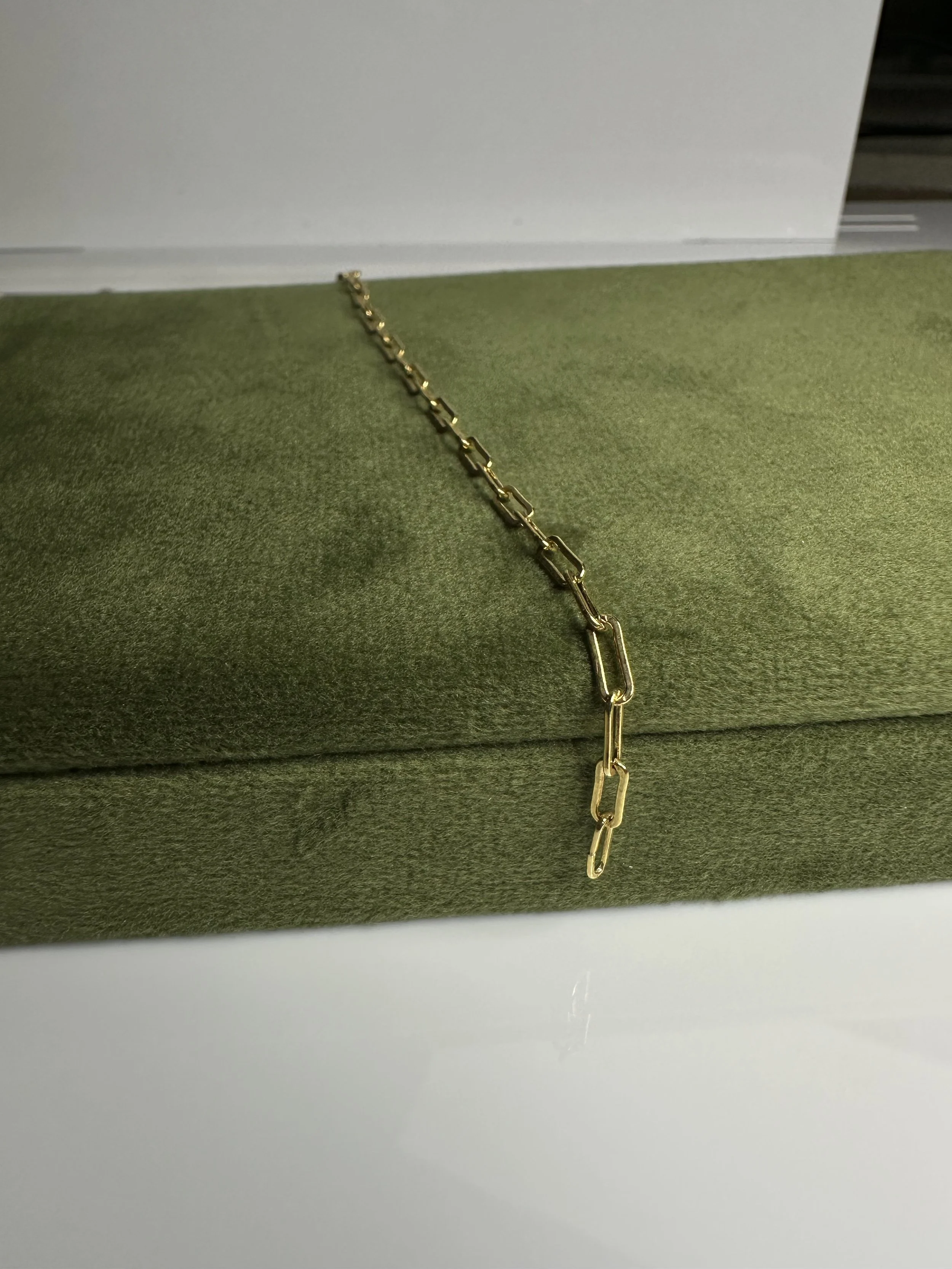 Gold chain necklace draped over a green velvet jewelry box.