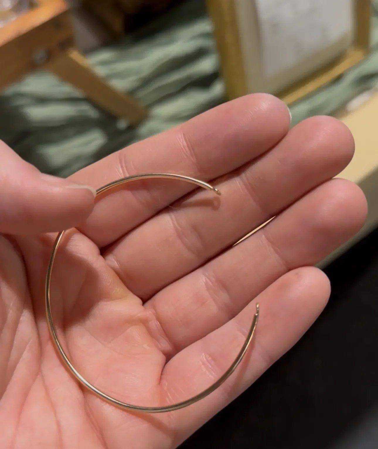 A person holding a gold bangle bracelet in their hand.