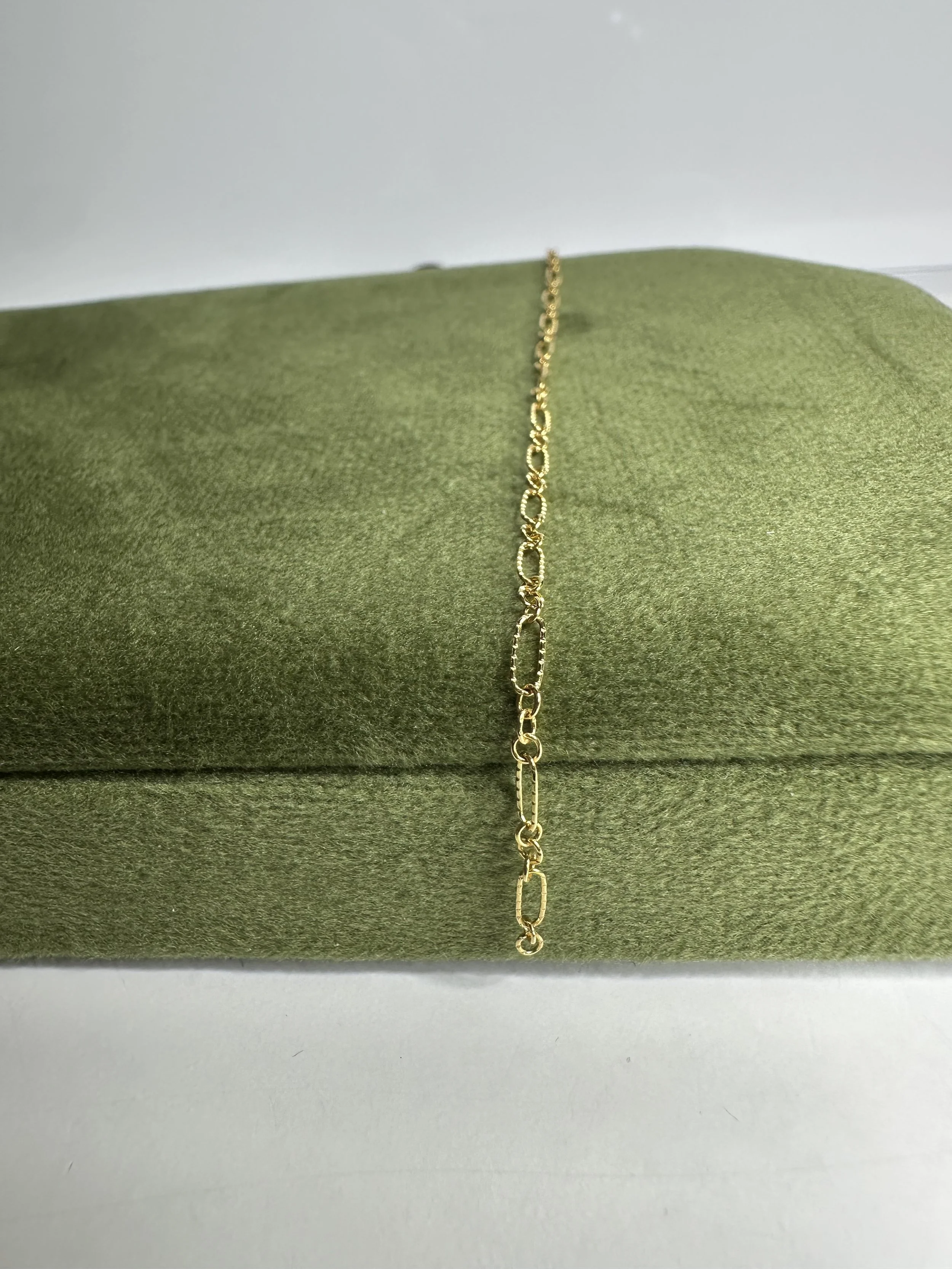 Gold chain necklace draped over a green velvet pillow.