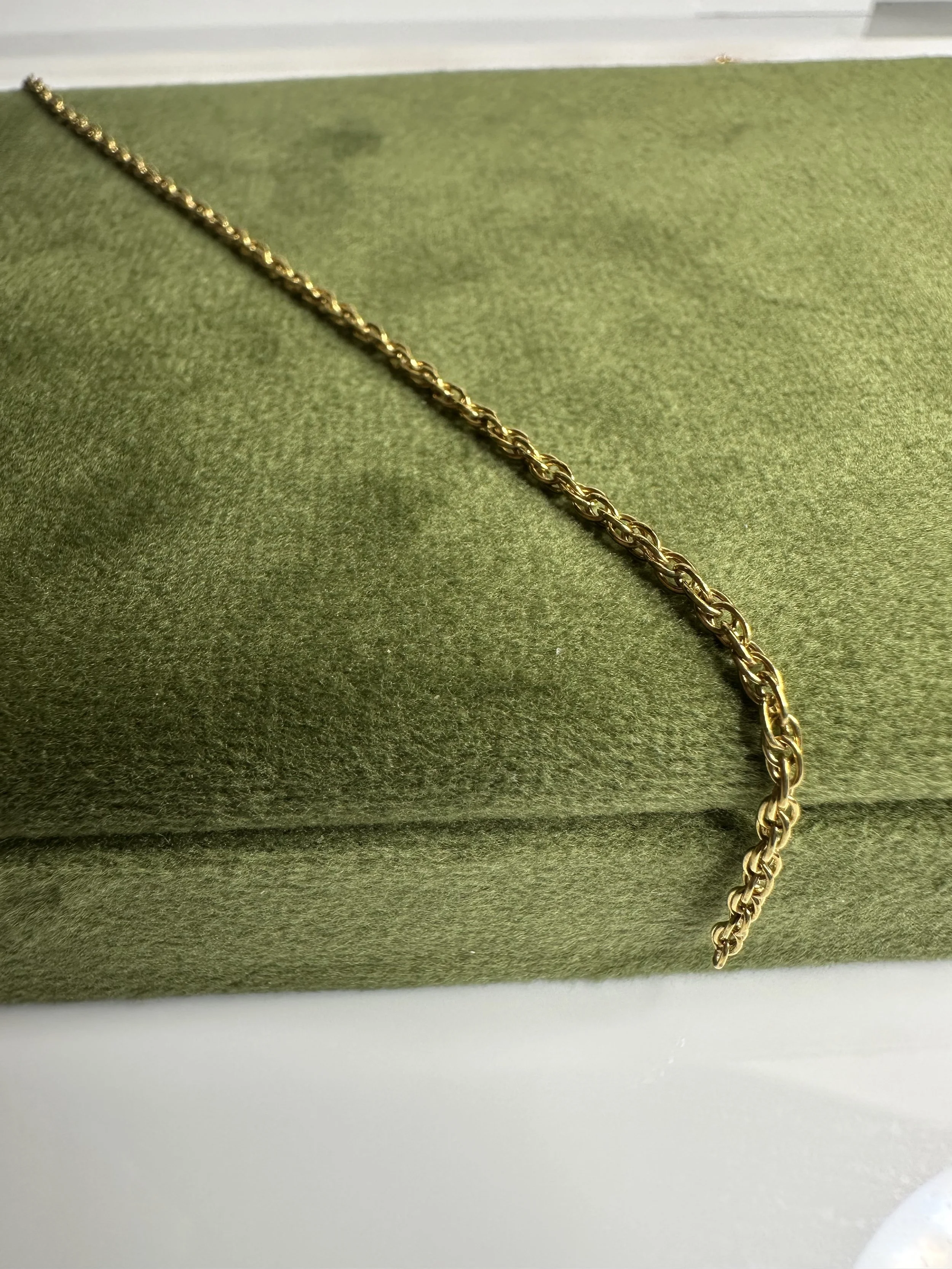 Gold chain necklace displayed on a green velvet surface.