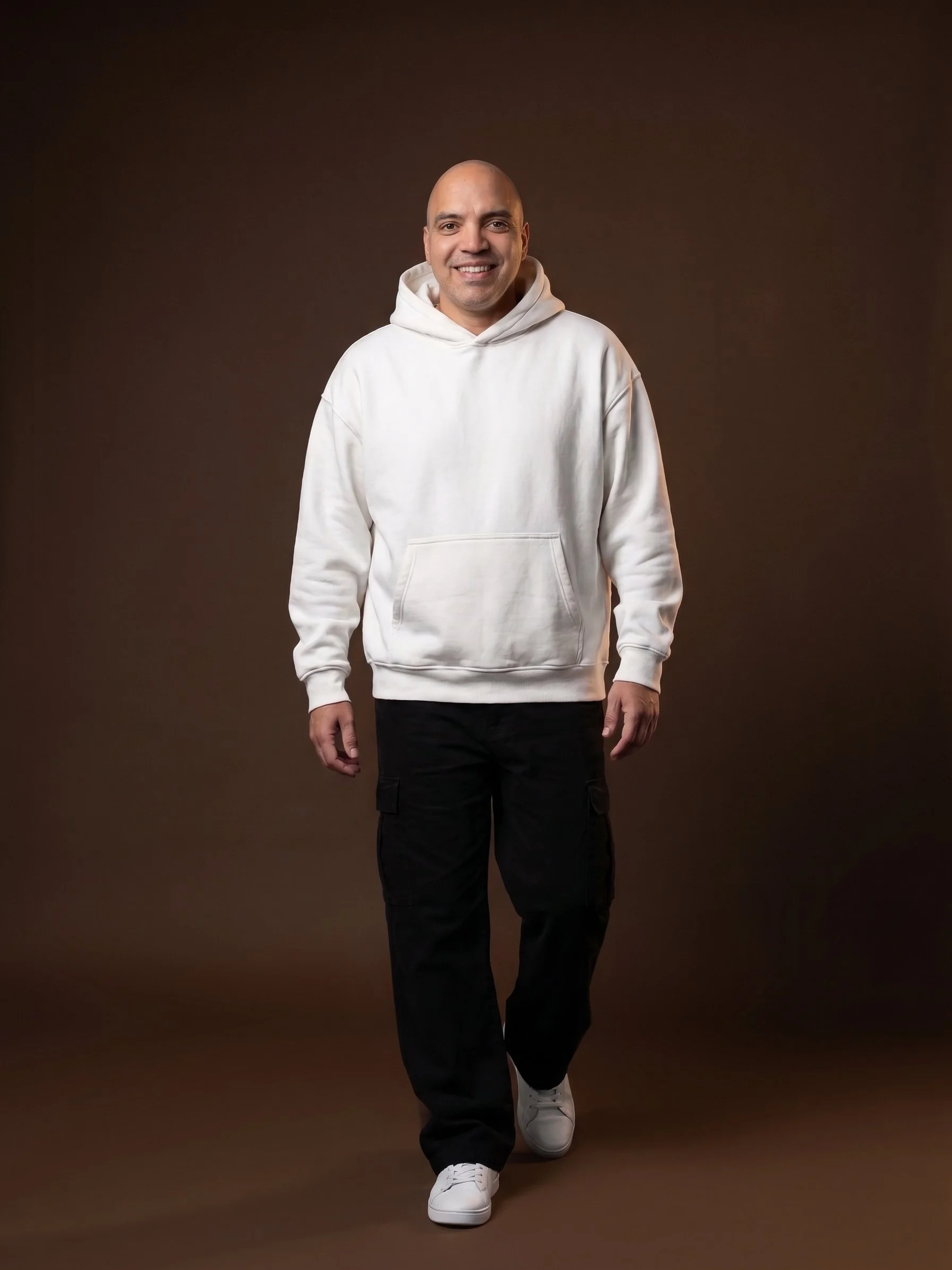 Orlando Nord, Reinvention Mentor, smiling in a white hoodie against a warm brown studio background