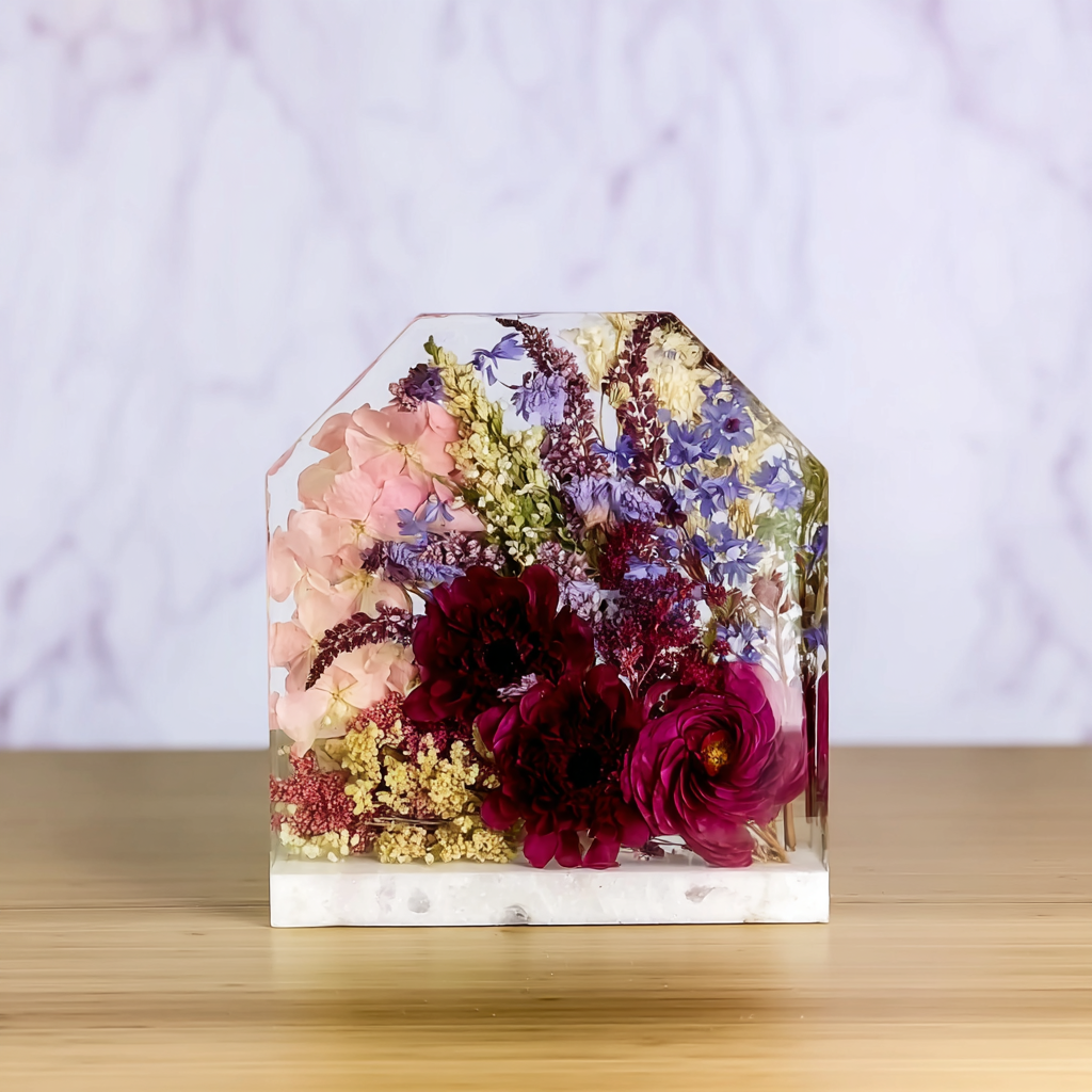 Wedding Bouquet Preservation - A clear resin block filled with various colorful flowers including pink, purple, yellow, and deep red, placed on a light wooden surface with a blurred light-colored background.