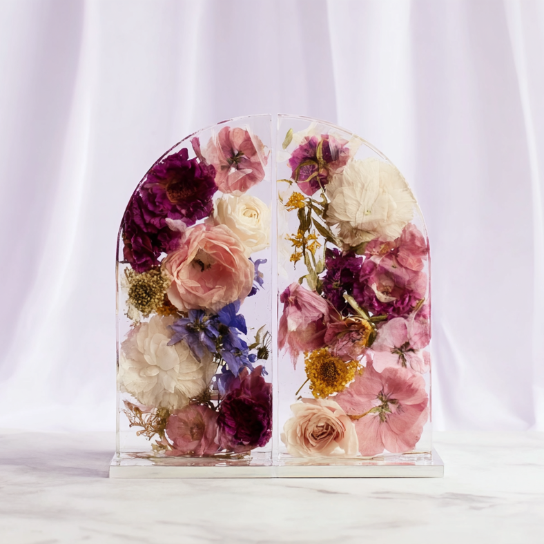 Custom flower preservation - A decorative resin frame filled with pressed and dried pink, white, purple, and yellow flowers on a white marble surface with white curtains in the background.