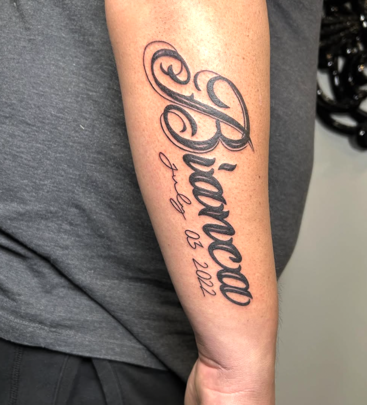 Tattoo on forearm with the name 'Valeria' in large cursive script and the phrase 'by 02.2022' in smaller cursive script underneath.