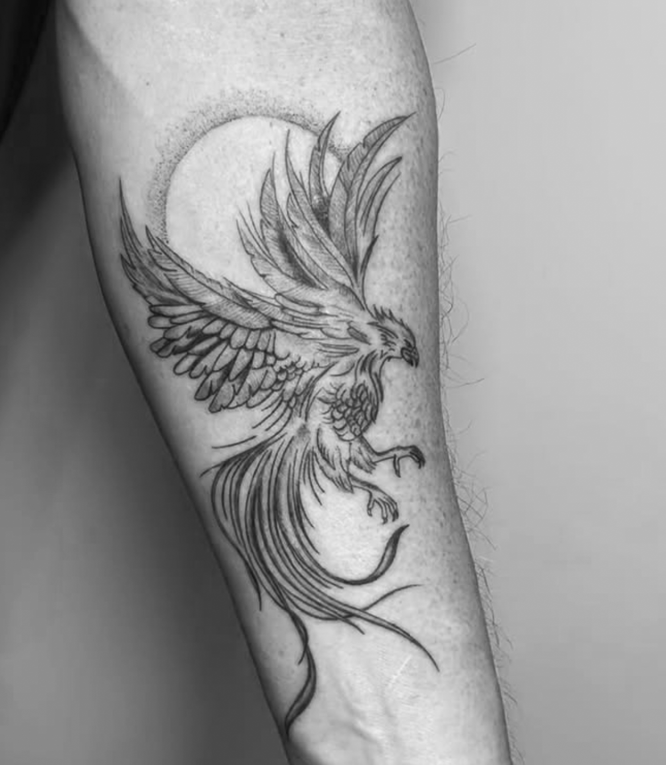 Tattoo of a detailed flying eagle with outstretched wings, talons, and a fish hook in black ink on a person's arm, with a full moon in the background.
