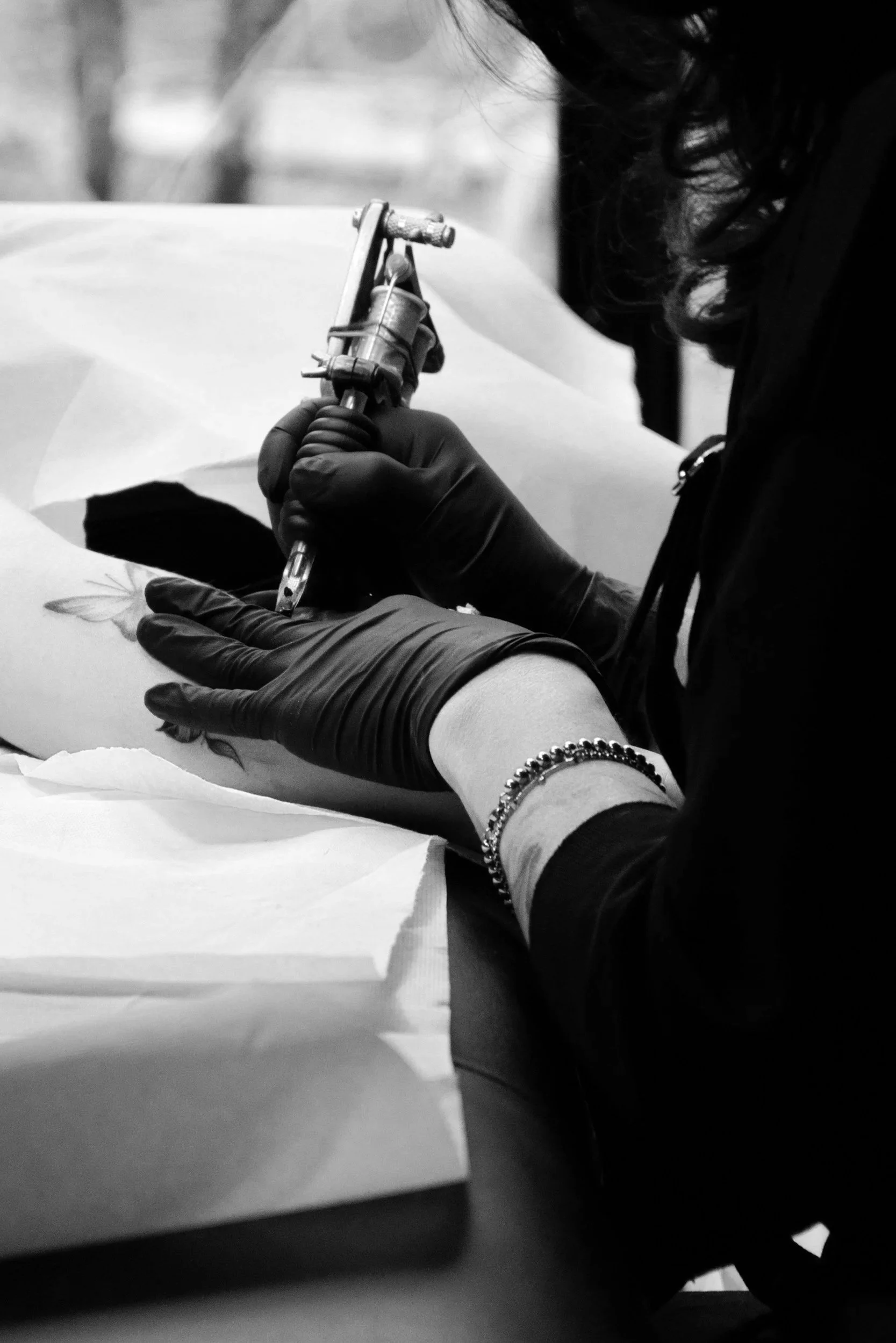 A person wearing black gloves is tattooing a design onto a client's arm using a tattoo machine.
