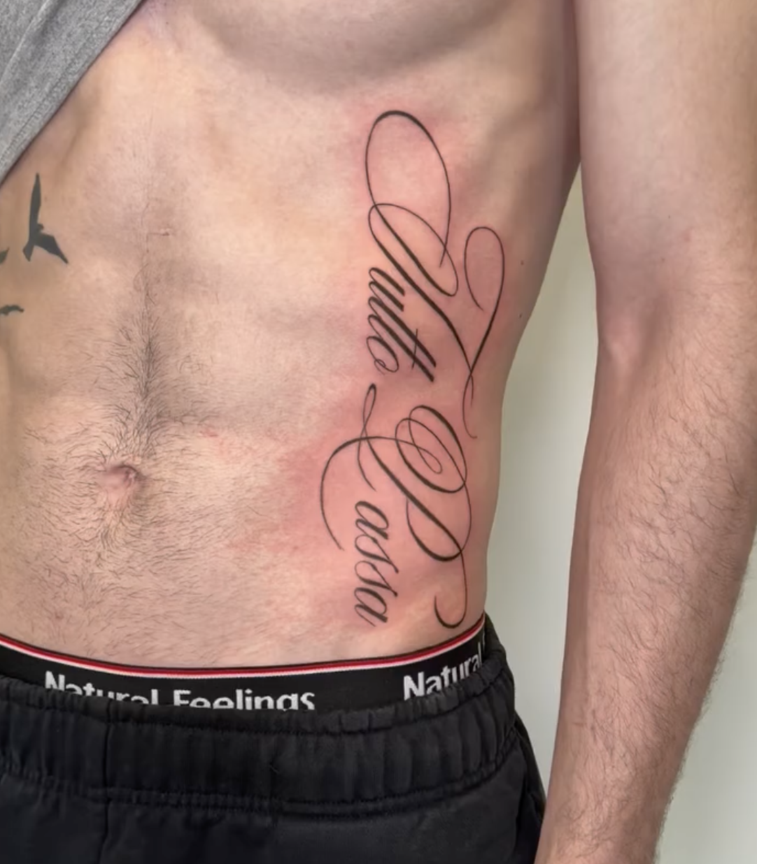 Tattoo on a man's side that reads 'Love' in cursive script.