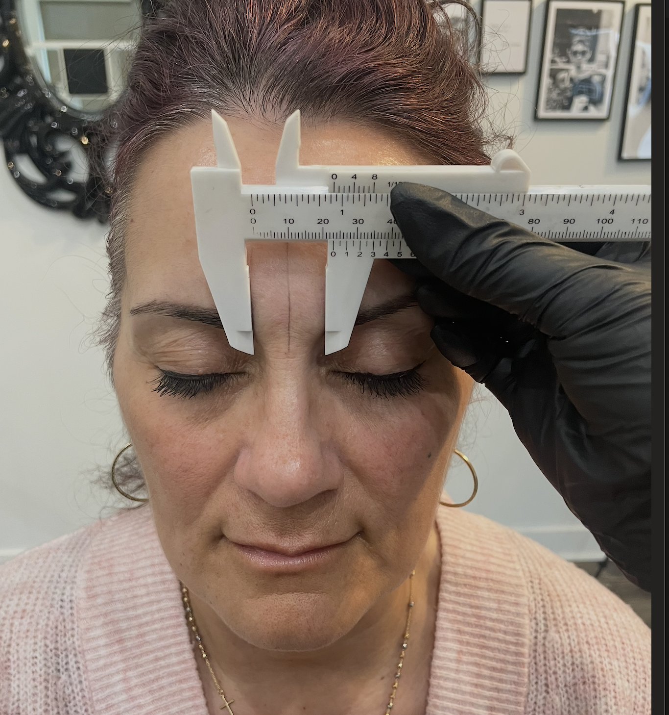 A woman with closed eyes has her forehead measured with a caliper by a person wearing a black glove.