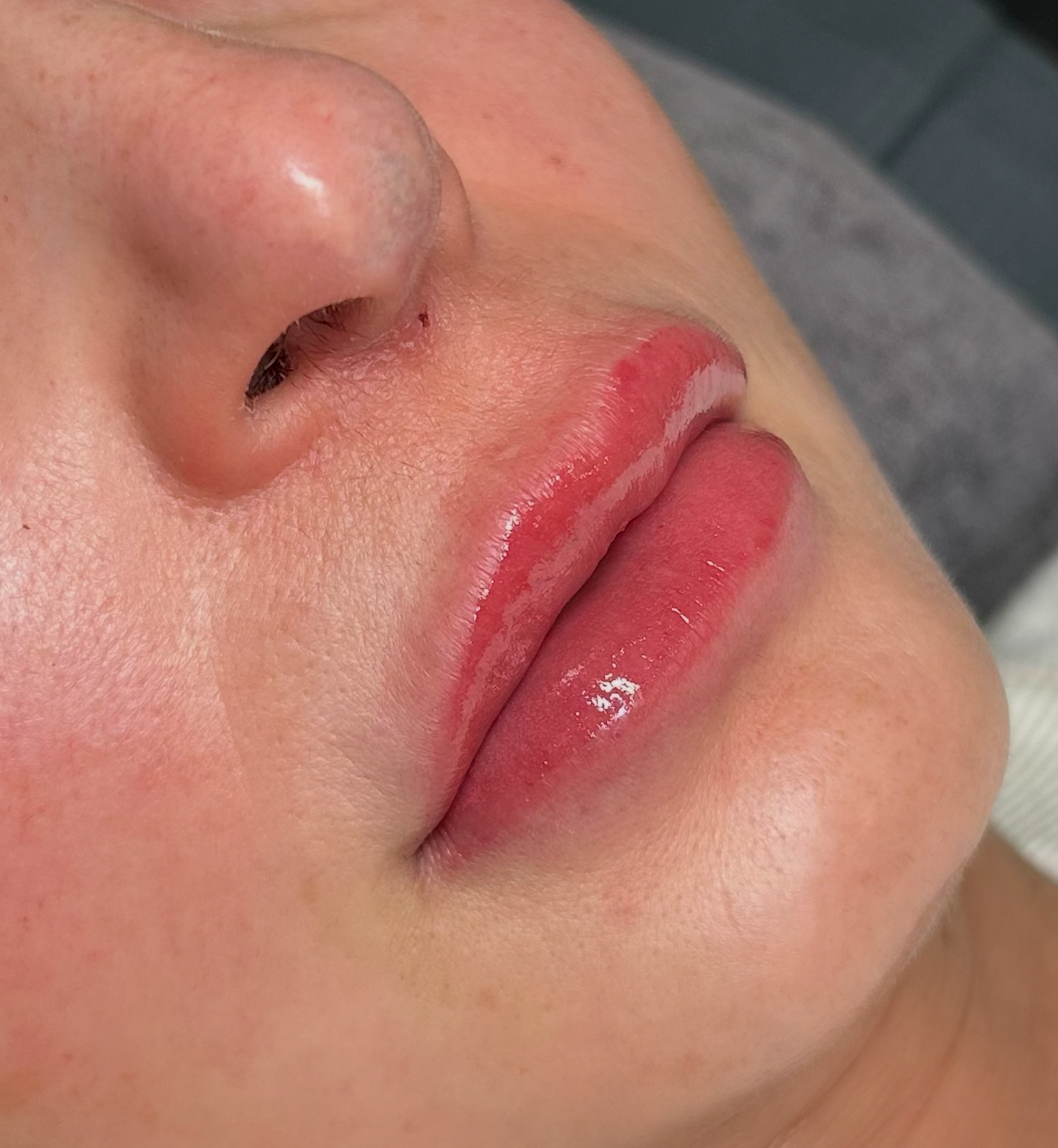 Close-up of a person's lips and nose, with lips slightly parted and glossy, showing a natural skin tone.