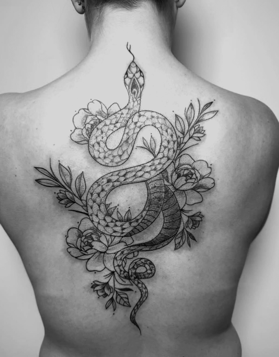 Black and white tattoo of a snake intertwined with flowers on a person's back.