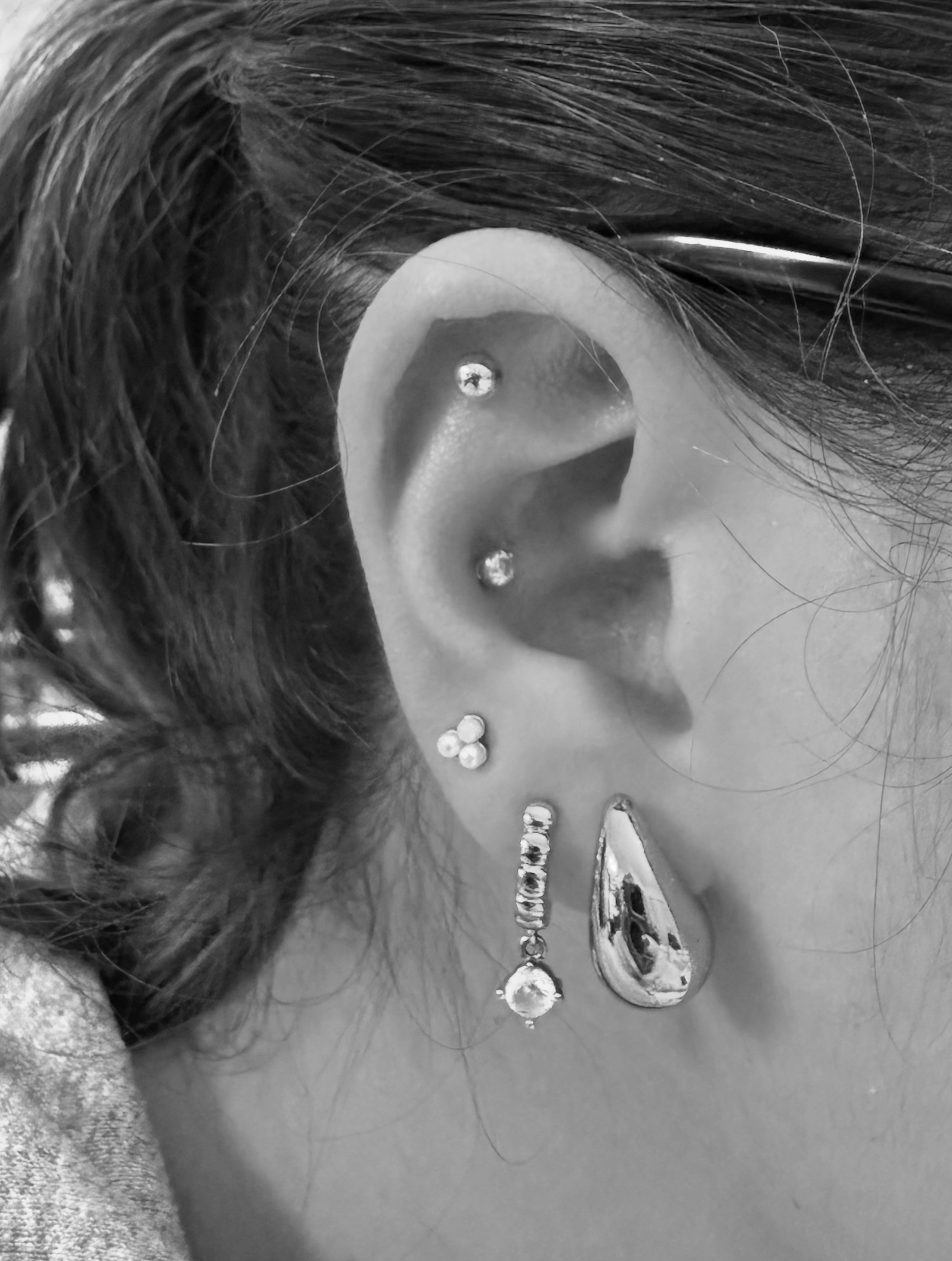 Close-up of a person's ear with multiple piercings and a cascade of earrings, with hair visible around the ear.
