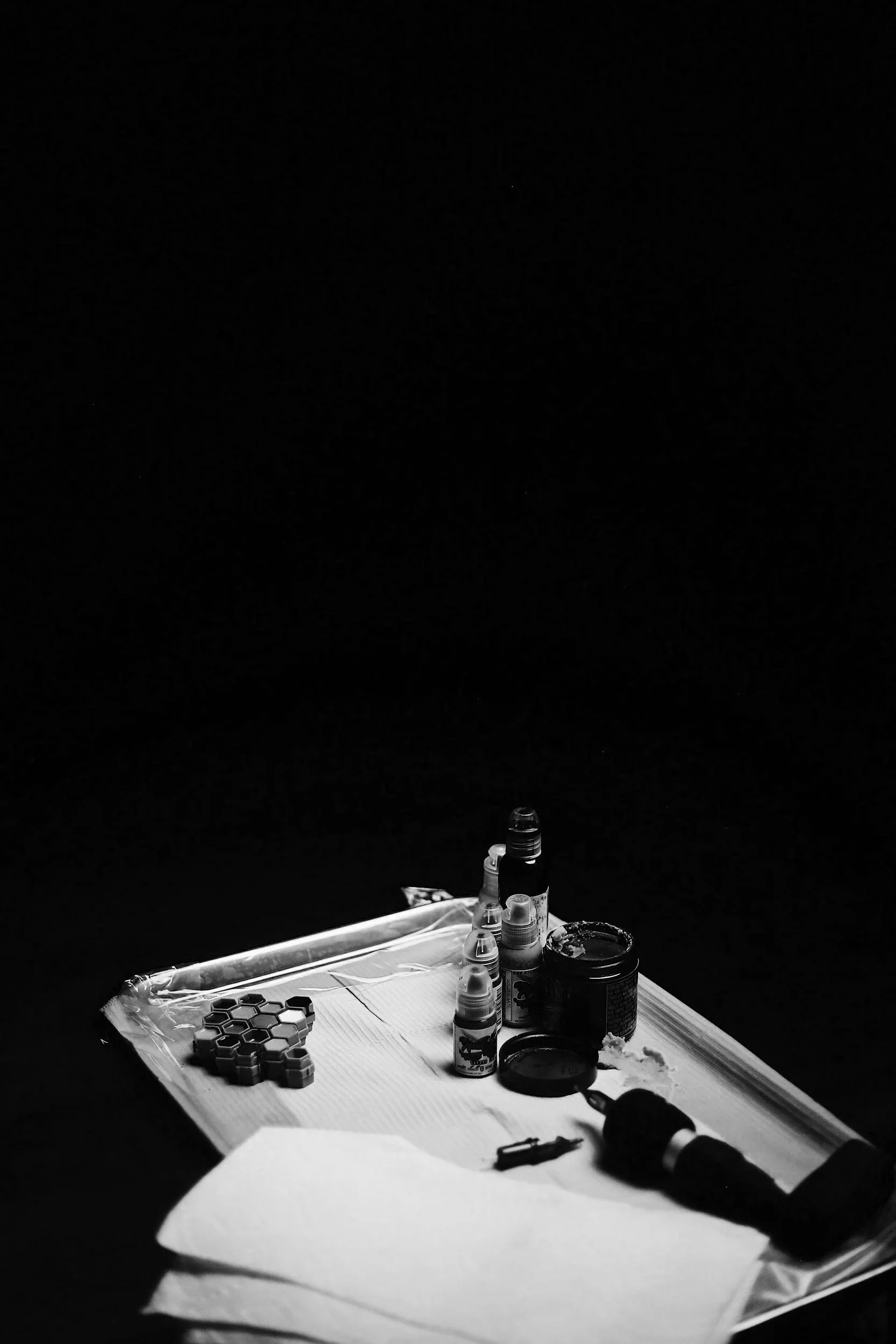 A scientific workspace with small bottles of ink or dye, a microscope, honeycomb-shaped objects, containers, and paper on a light-colored tray against a black background.