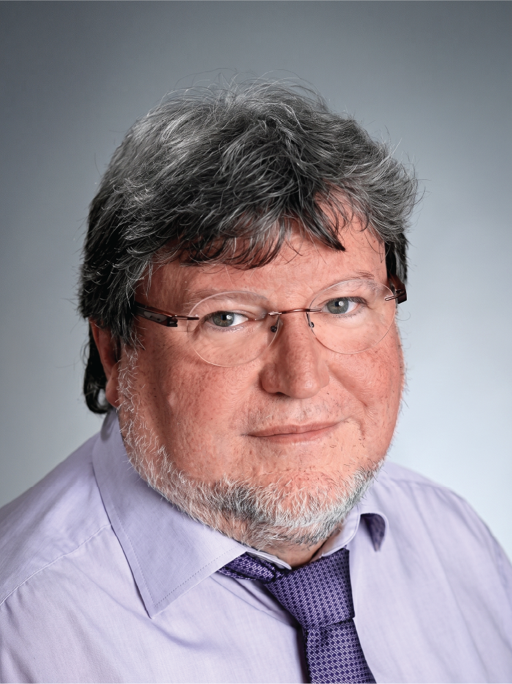 Dr Alfons Meyer, a middle-aged man with grey hair, glasses, and a beard, wearing a light purple shirt and a purple tie.