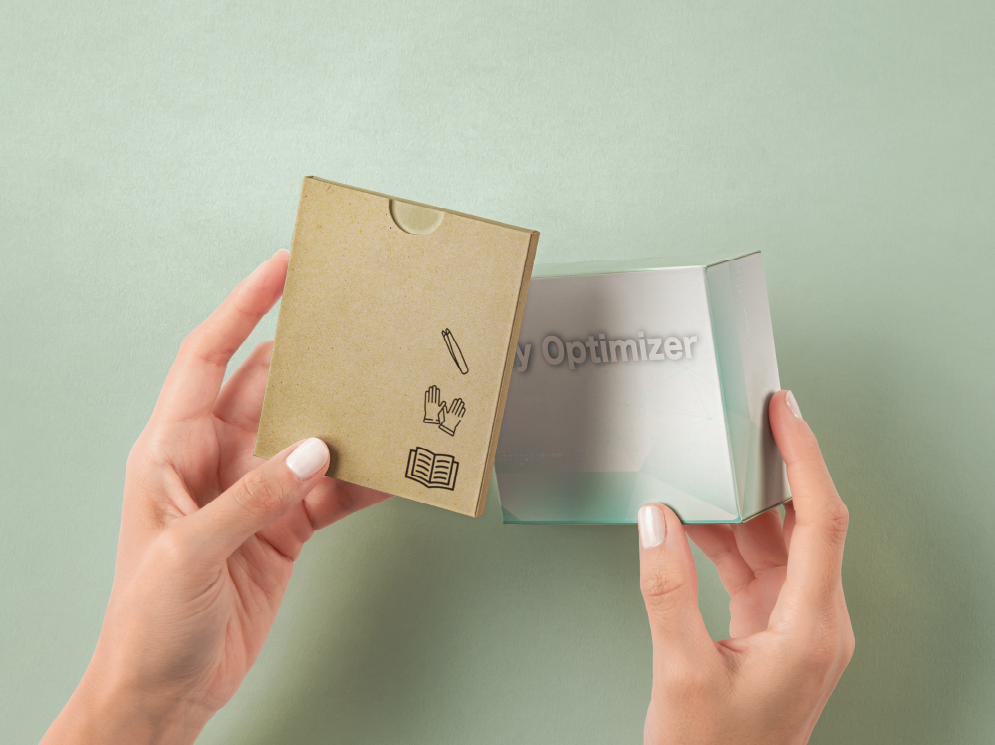 Hands opening a small box labeled "My Optimizer" with instructions printed on its flap, including icons of a pen, gloves, and a book, against a light green background.
