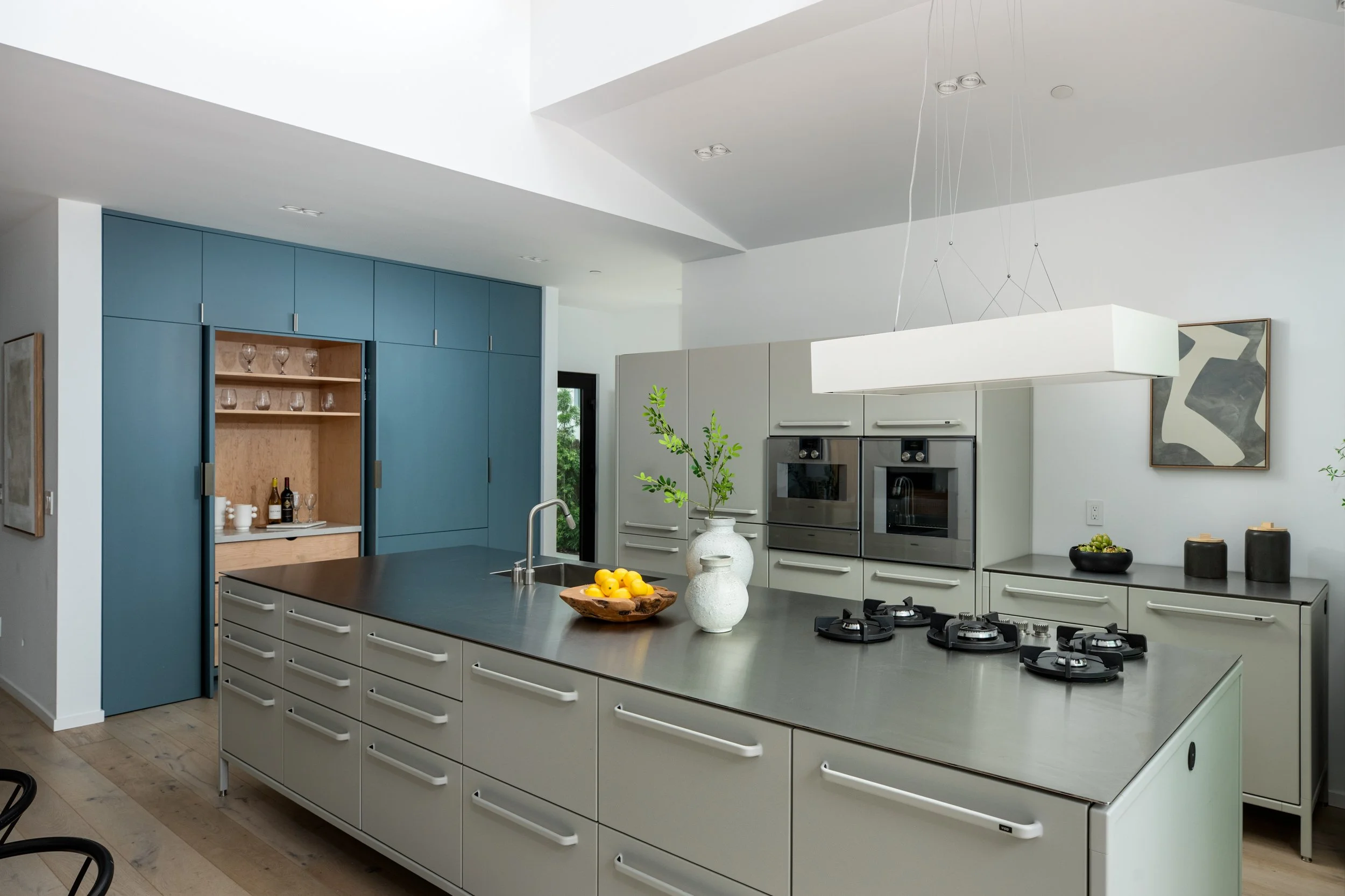 Modern kitchen with a large kitchen island, overhead lighting, white and blue cabinetry, and decor including vases and bowls with lemons.