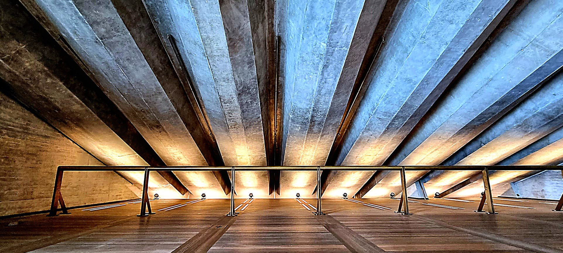 Looking up at a wooden ceiling with metal beams and warm lighting at the base of a modern staircase with metal railings.