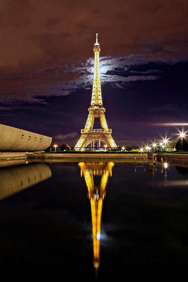 The Eiffel Tower illuminated at night, reflected in a body of water in Paris, France.