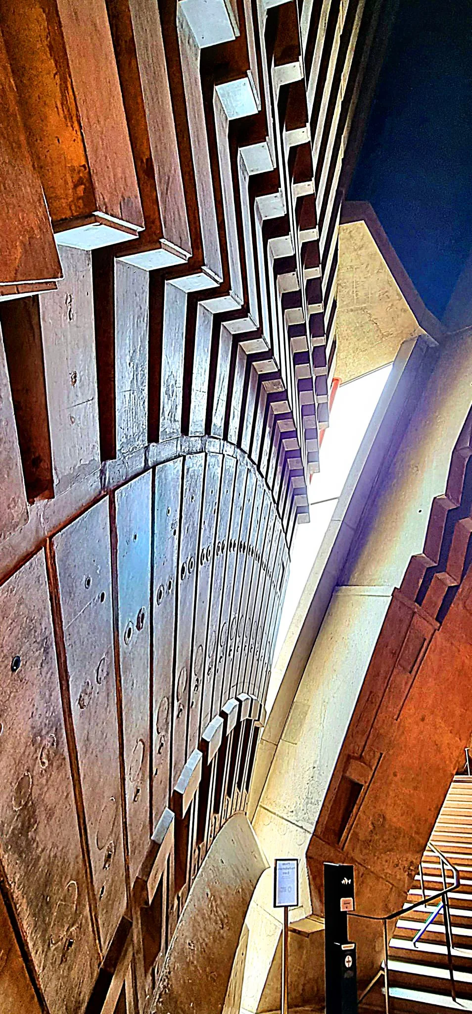 Interior view of a museum display with rows of large, curved, wooden architectural elements and stairs in the background.