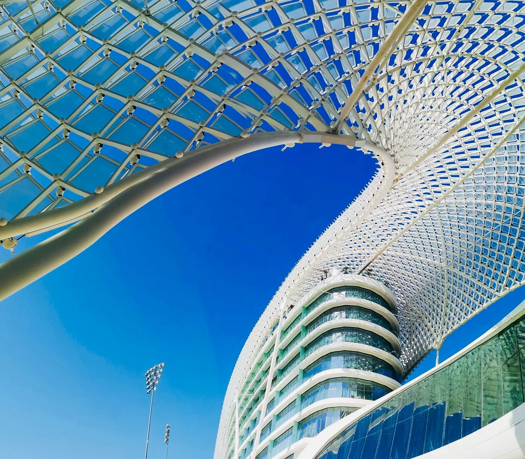 Modern architectural building with a curved design, featuring glass windows and a patterned, lattice-like roof structure against a clear blue sky.