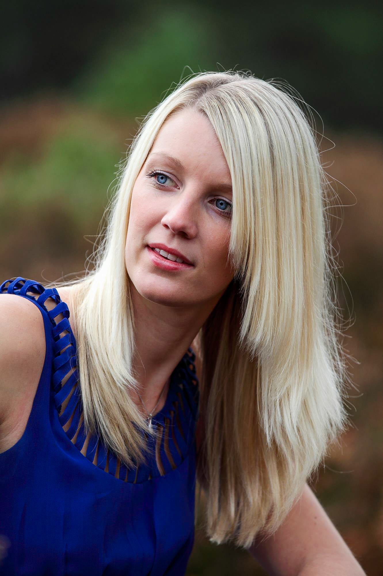 A woman with long blonde hair wearing a sleeveless blue top outdoors
